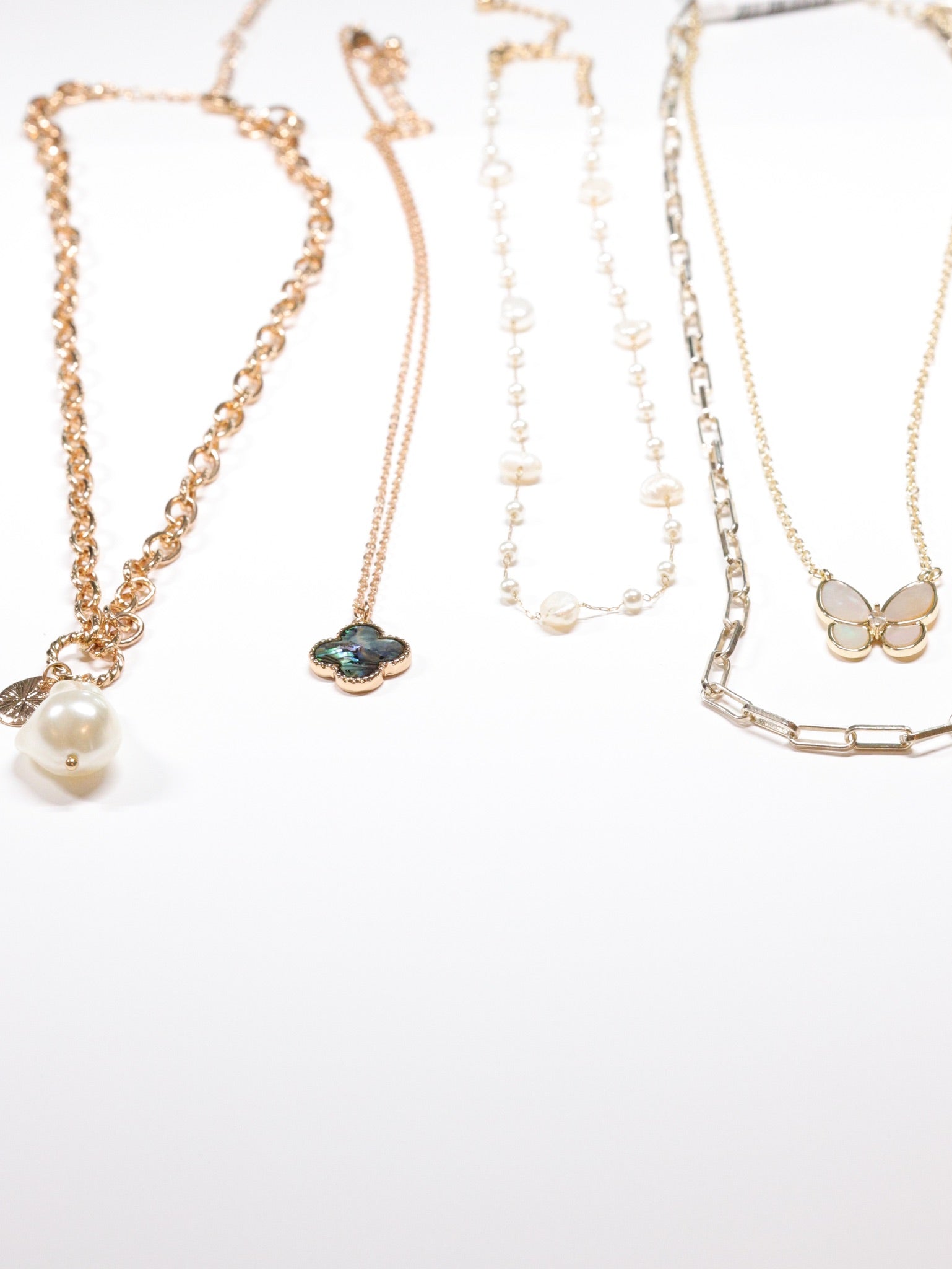 Gold and silver chain necklaces with pearl, clover, and butterfly pendants from Ardor Boutique’s layered necklace collection