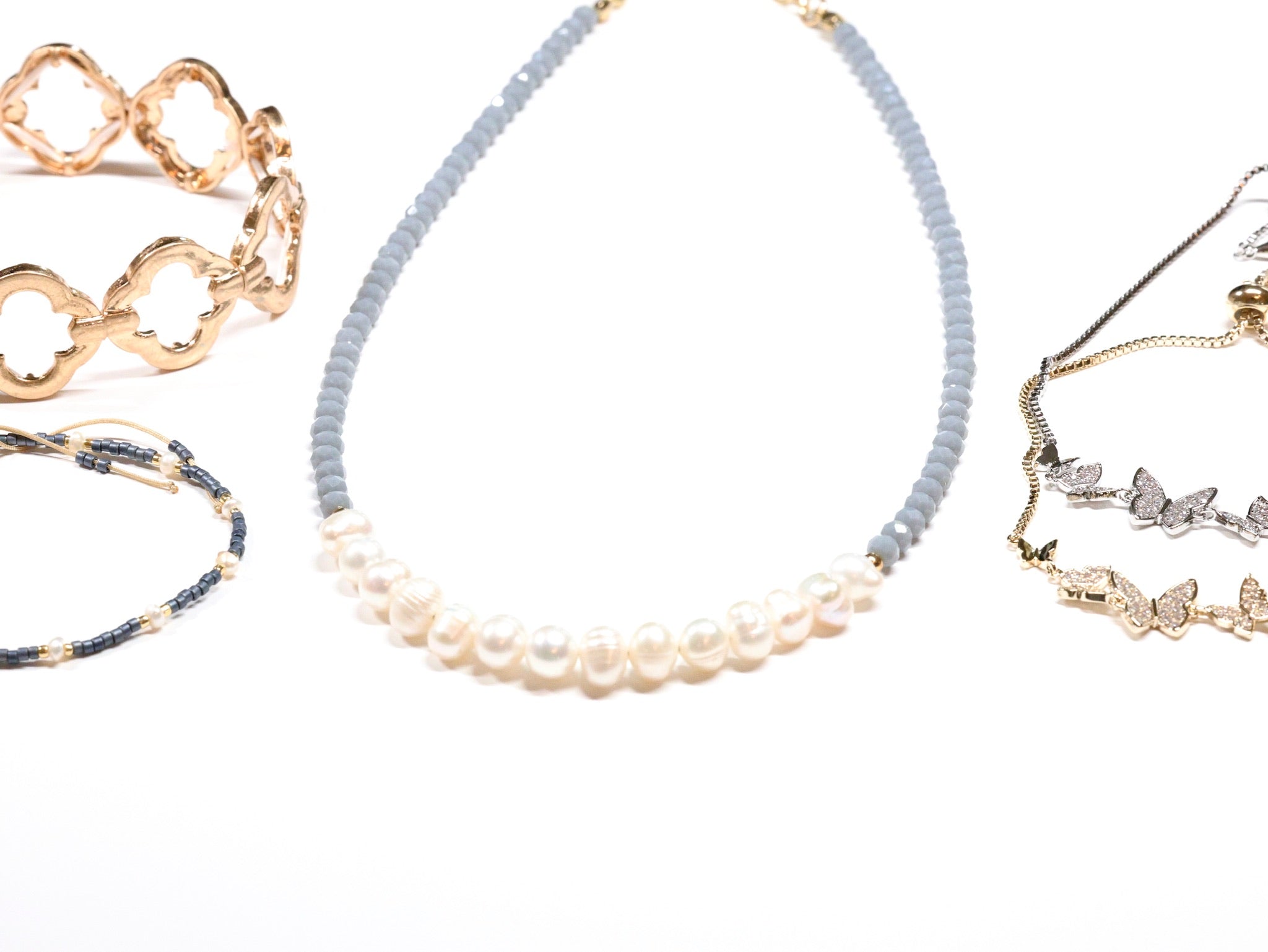 Assorted jewelry including pearl and bead necklace, gold cuff bracelet, and butterfly charm bracelets from Ardor Boutique