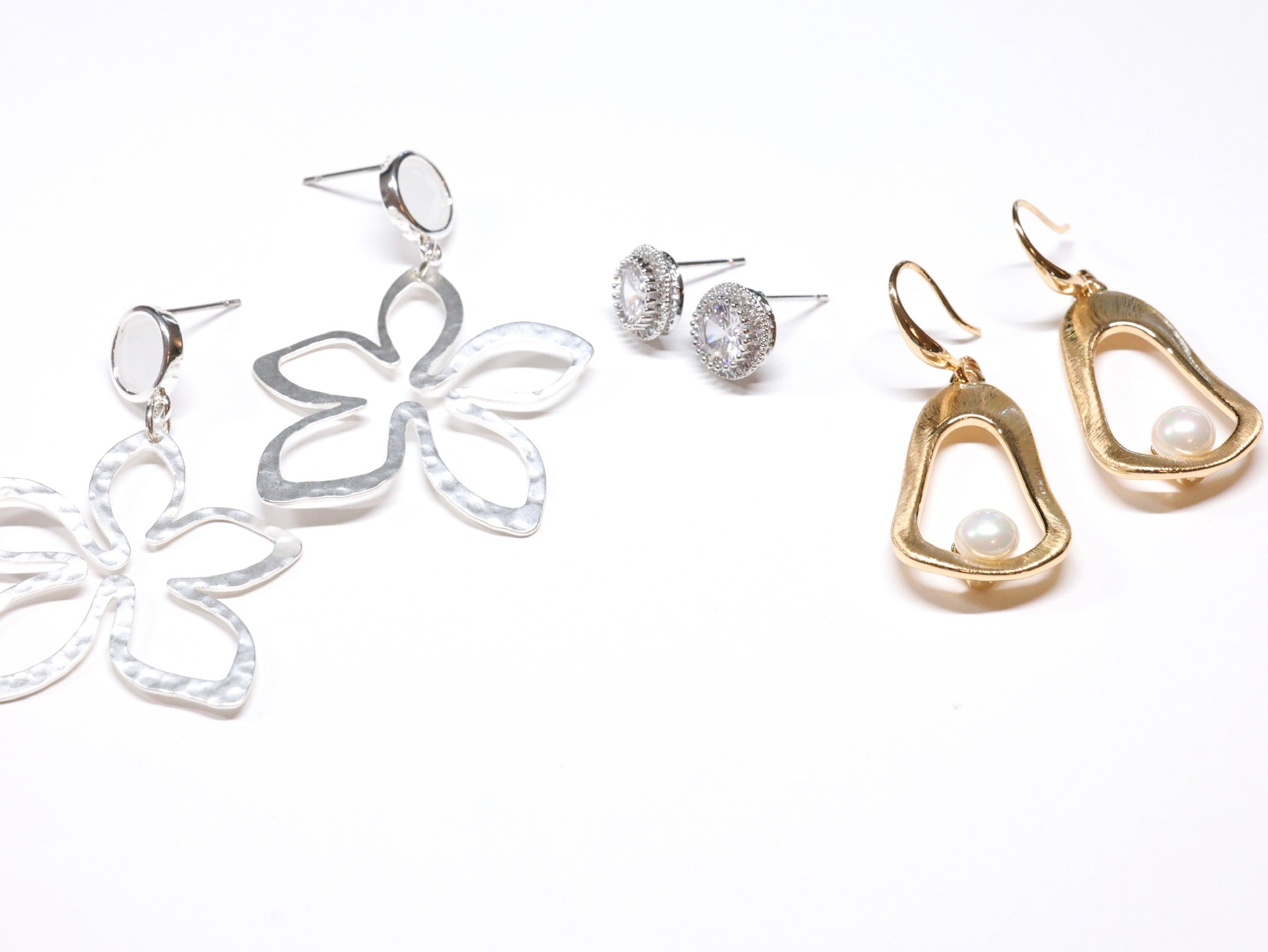 Assorted statement earrings including silver floral drops, crystal studs, and gold pearl dangles from Ardor Boutique