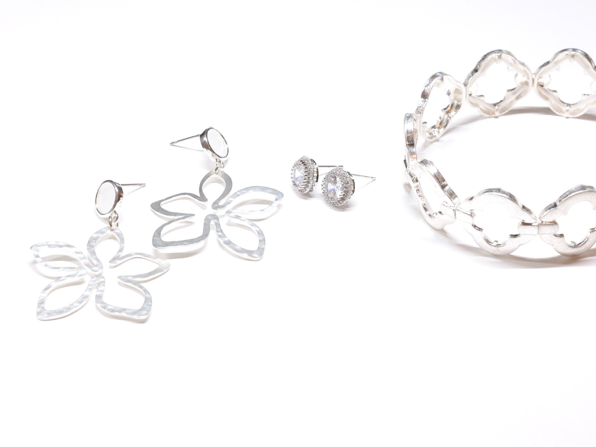 Silver jewelry set with dangly floral earrings, sparkly studs, and a clover stretch bracelet.
