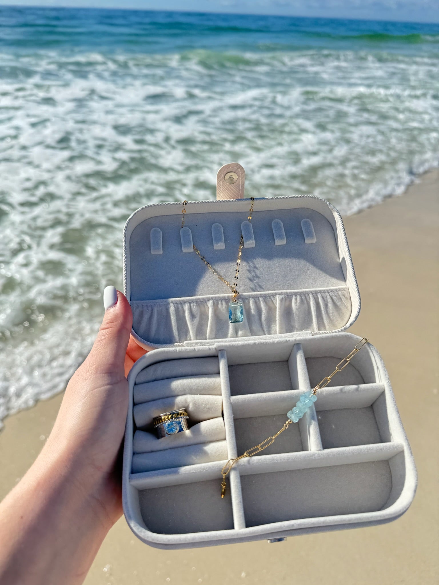 Gold and blue necklace, bracelet, and a ring in a jewelry box with ocean waves behind.