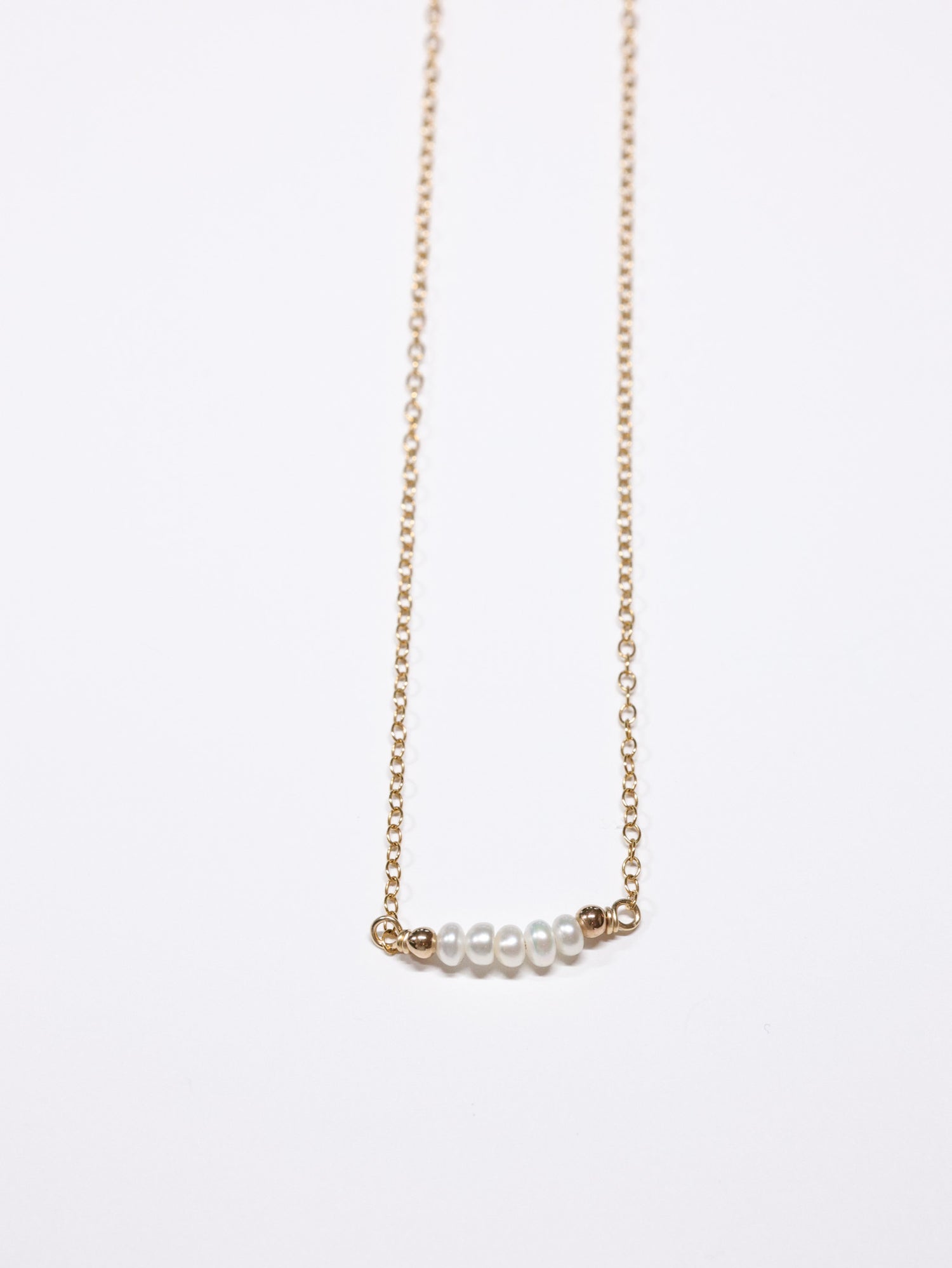 Minimalist gold chain necklace featuring a horizontal row of small white freshwater pearls framed by tiny gold beads. Elegant and dainty handmade piece from the Nina Halls collection.