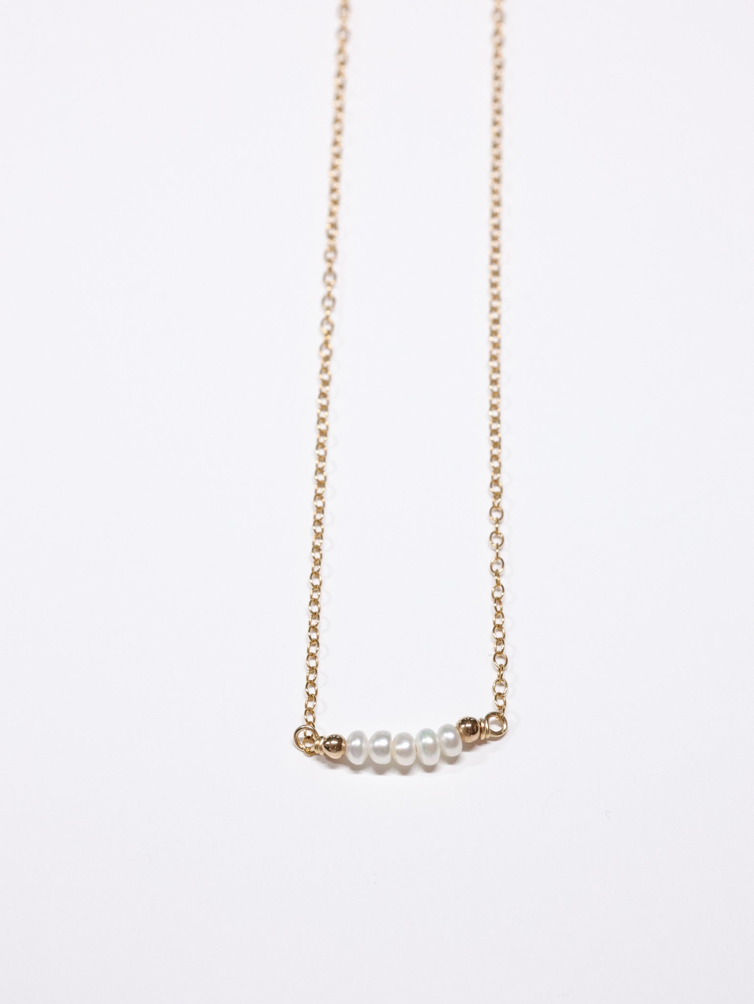 Minimalist gold chain necklace featuring a horizontal row of small white freshwater pearls framed by tiny gold beads. Elegant and dainty handmade piece from the Nina Halls collection.