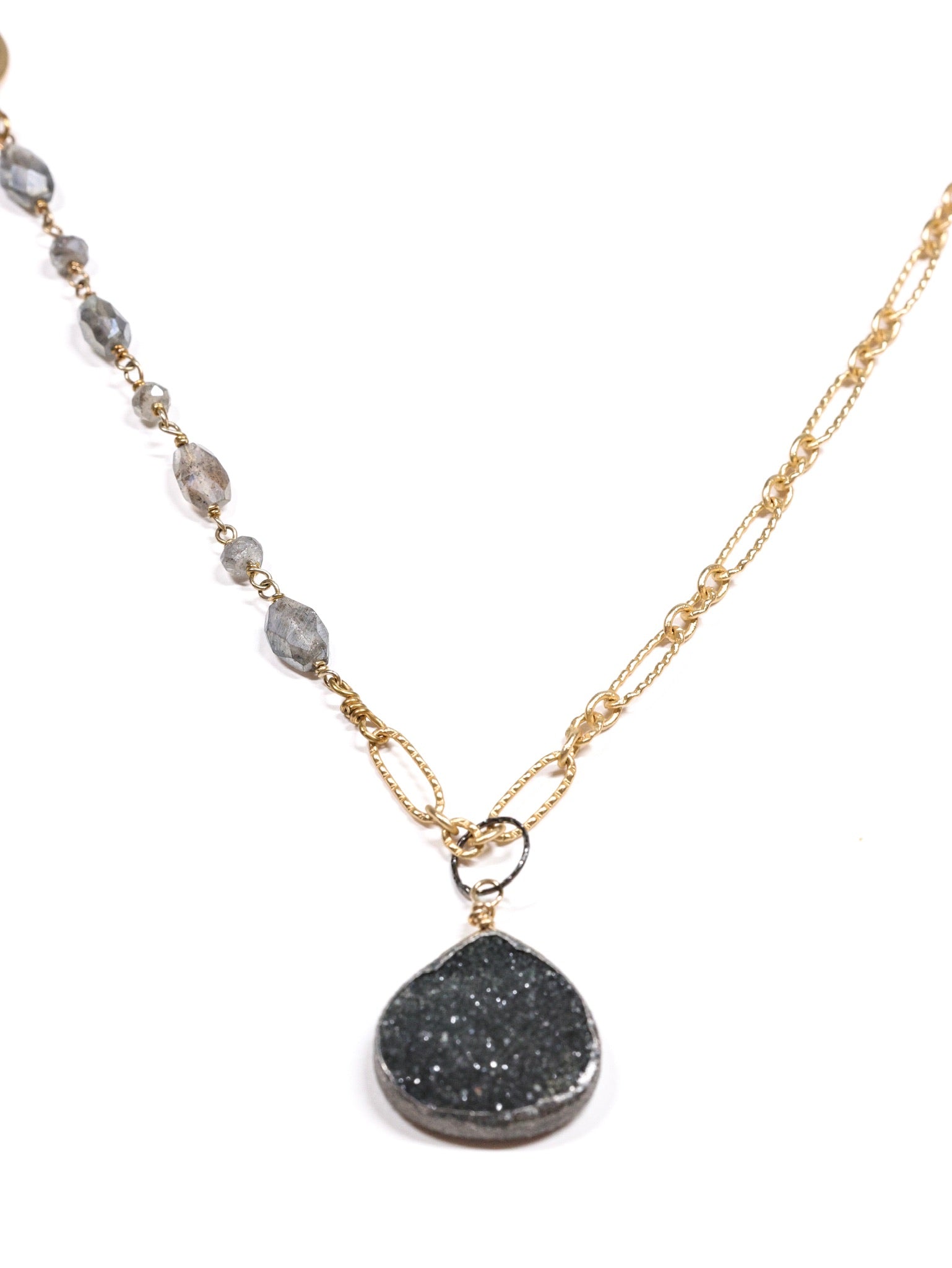 Close-up of a handmade necklace featuring labradorite beading on one side, gold-filled chain on the other, and a teardrop black druzy pendant.