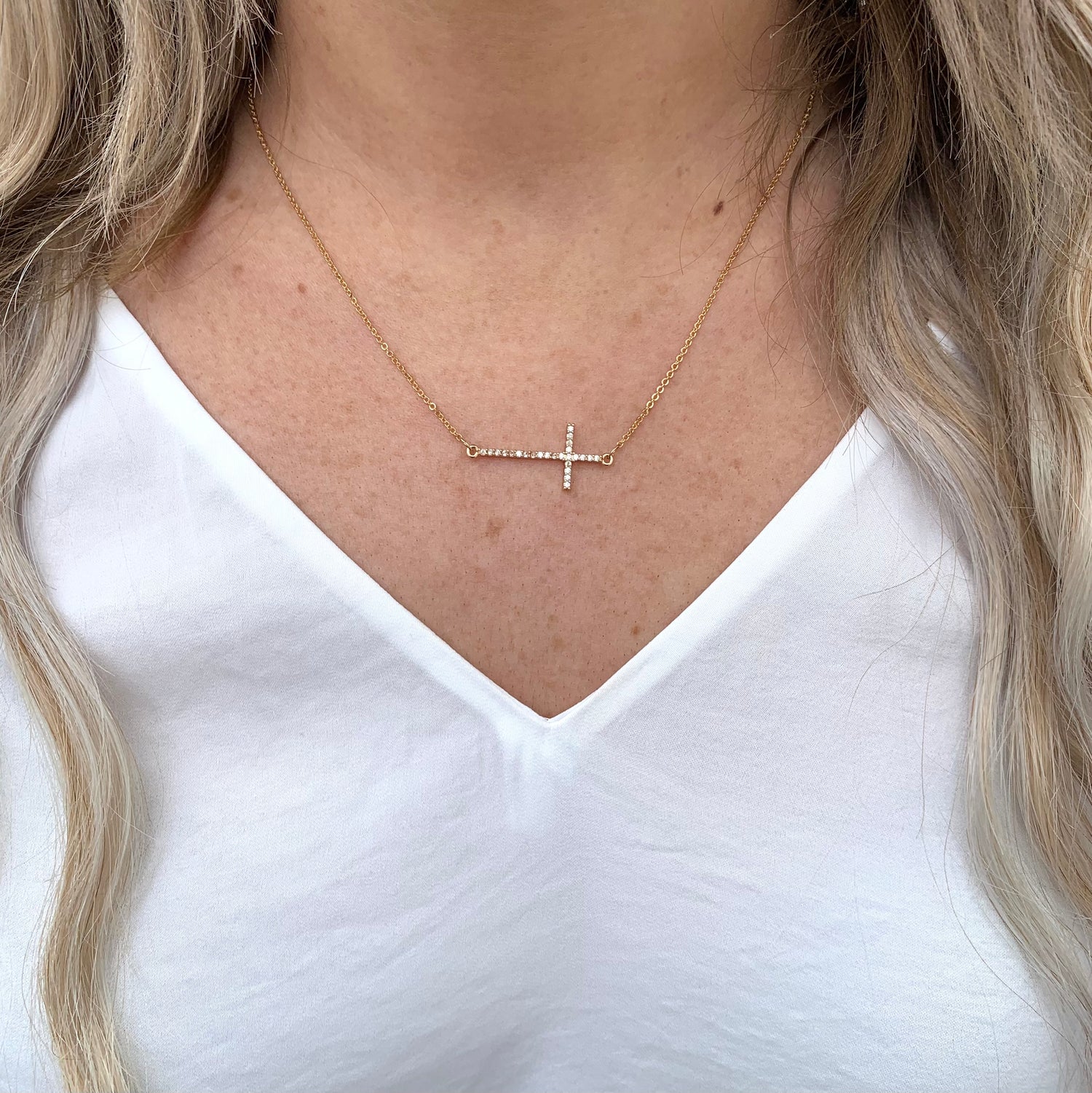 Gold sideways cross necklace on model.