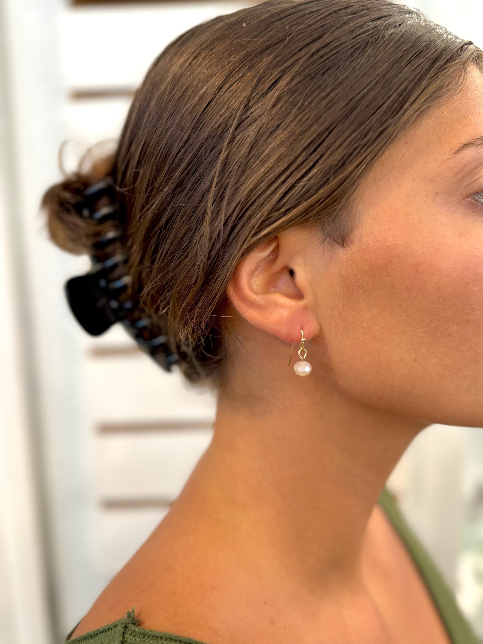 Close-up of a woman's ear with an earring, hair styled with clips, and blurred background.