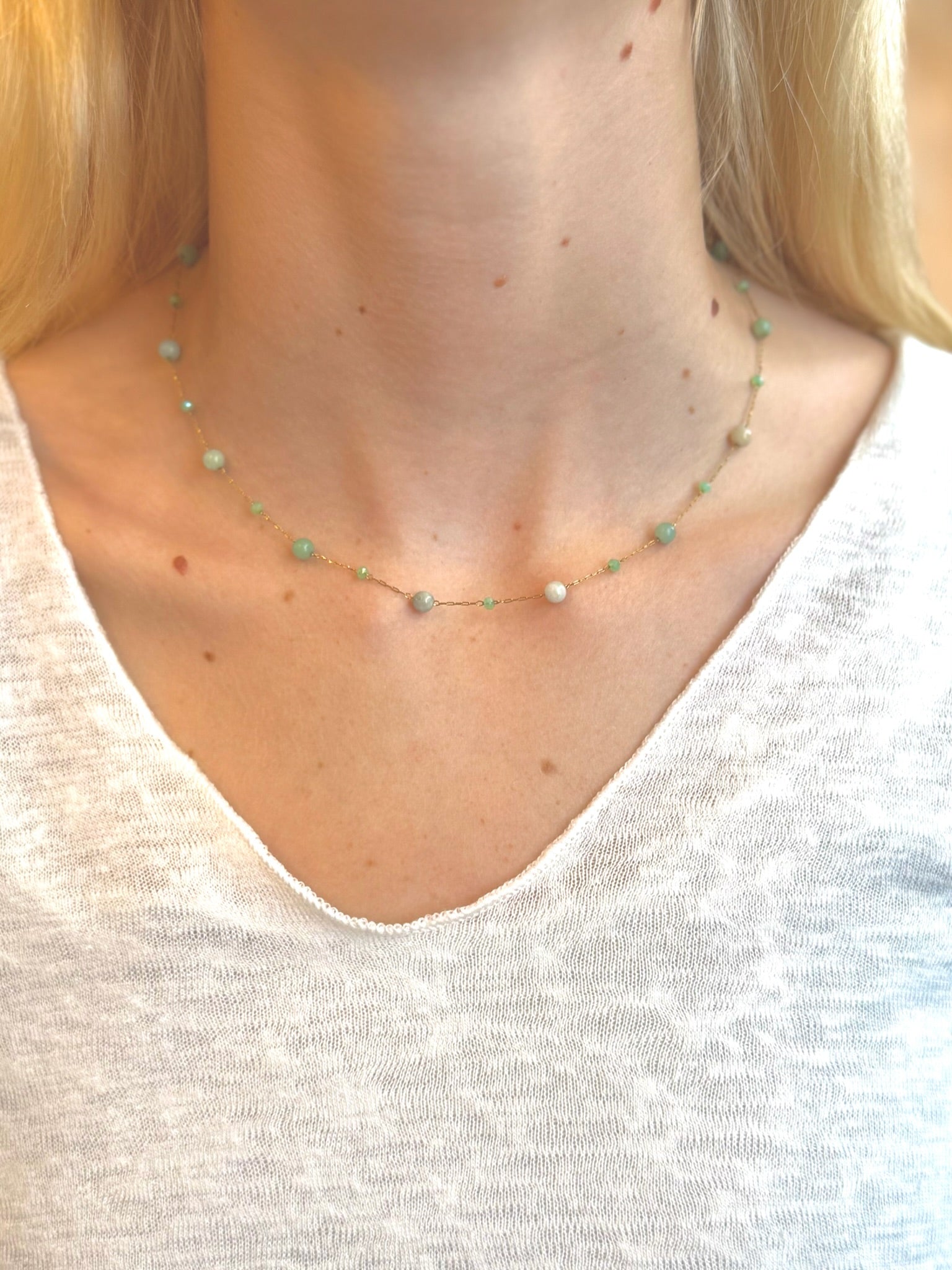 Green beaded gold chain necklace worn around neck, close-up view over a white shirt.