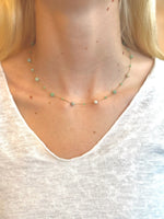 Model wearing necklace with small beads and a white shirt.