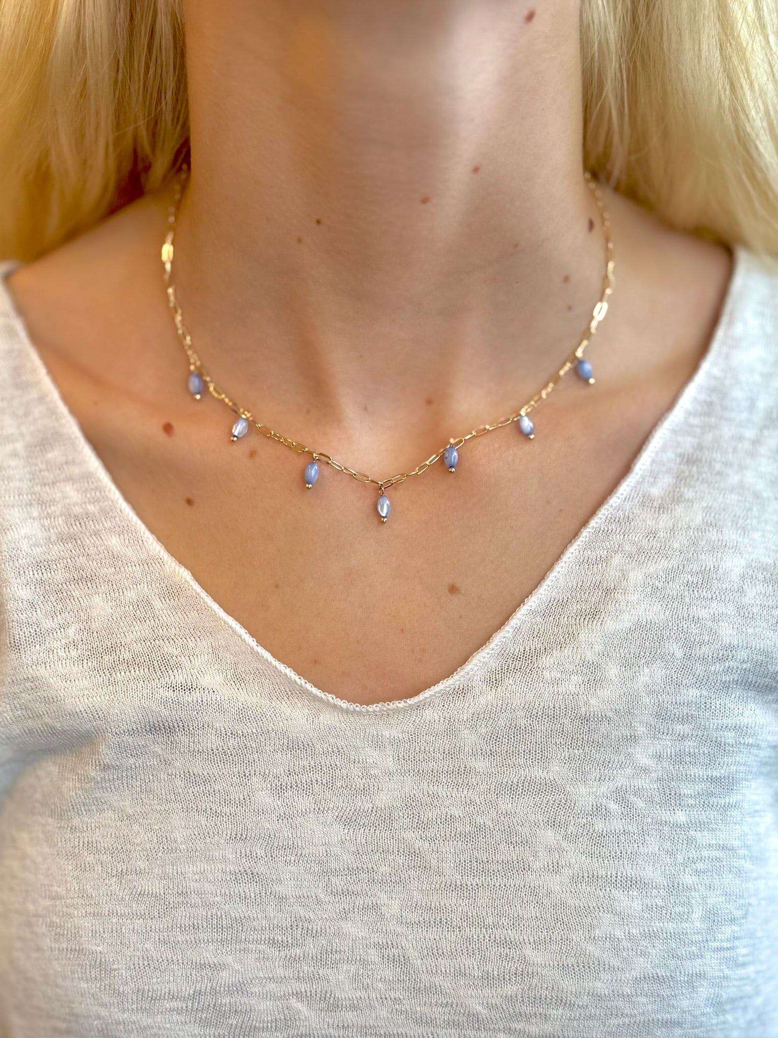 Woman wearing a gold necklace with dangling lavender bead accents, styled with a soft scoop-neck white top
