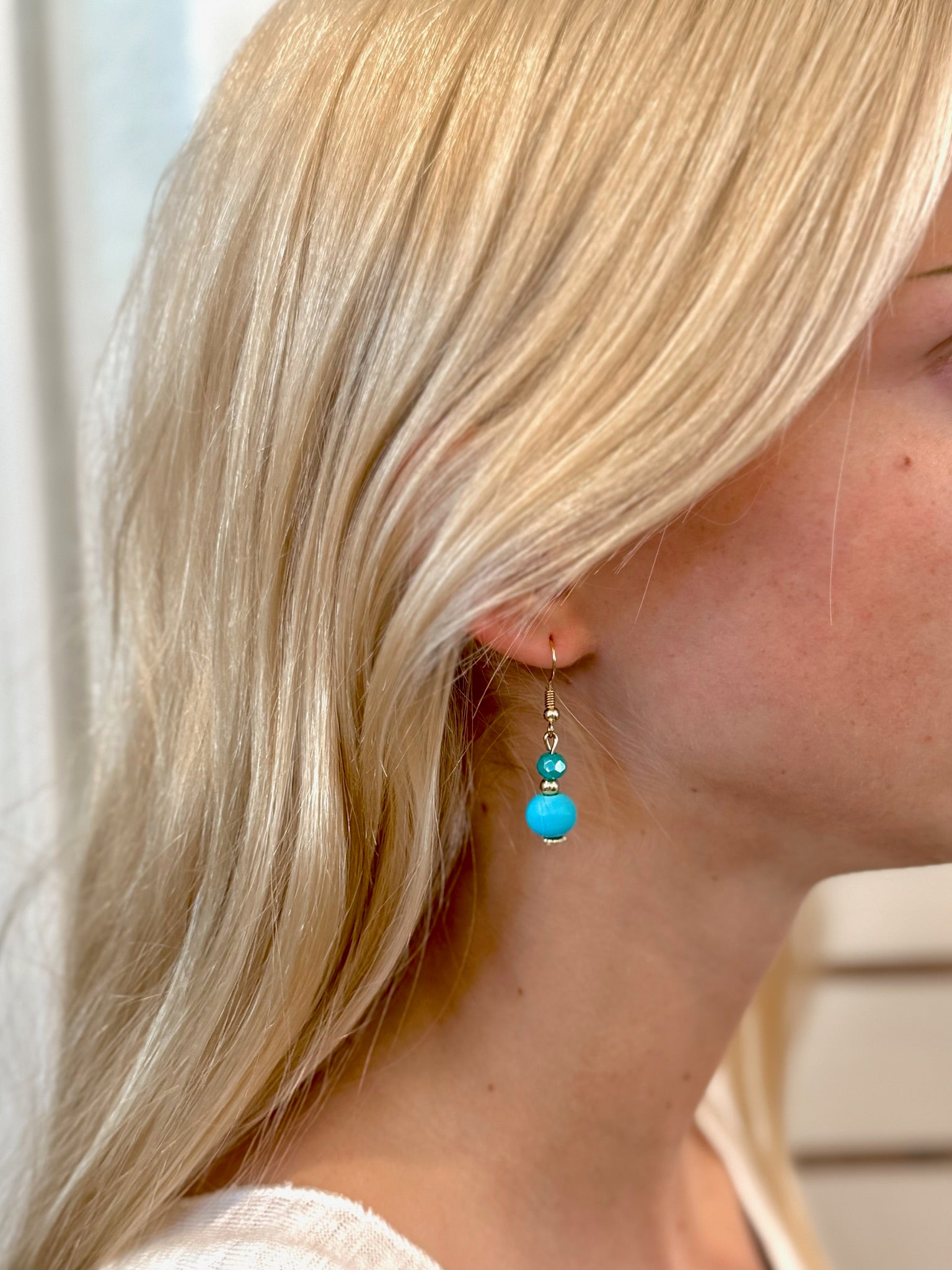 Woman wearing turquoise drop earrings with fabric and glass beads, gold hook detail