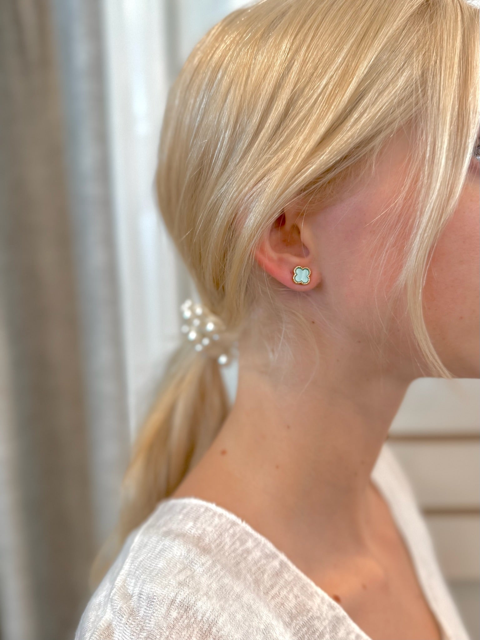 Close-up of woman wearing light blue clover stud earrings with gold trim
