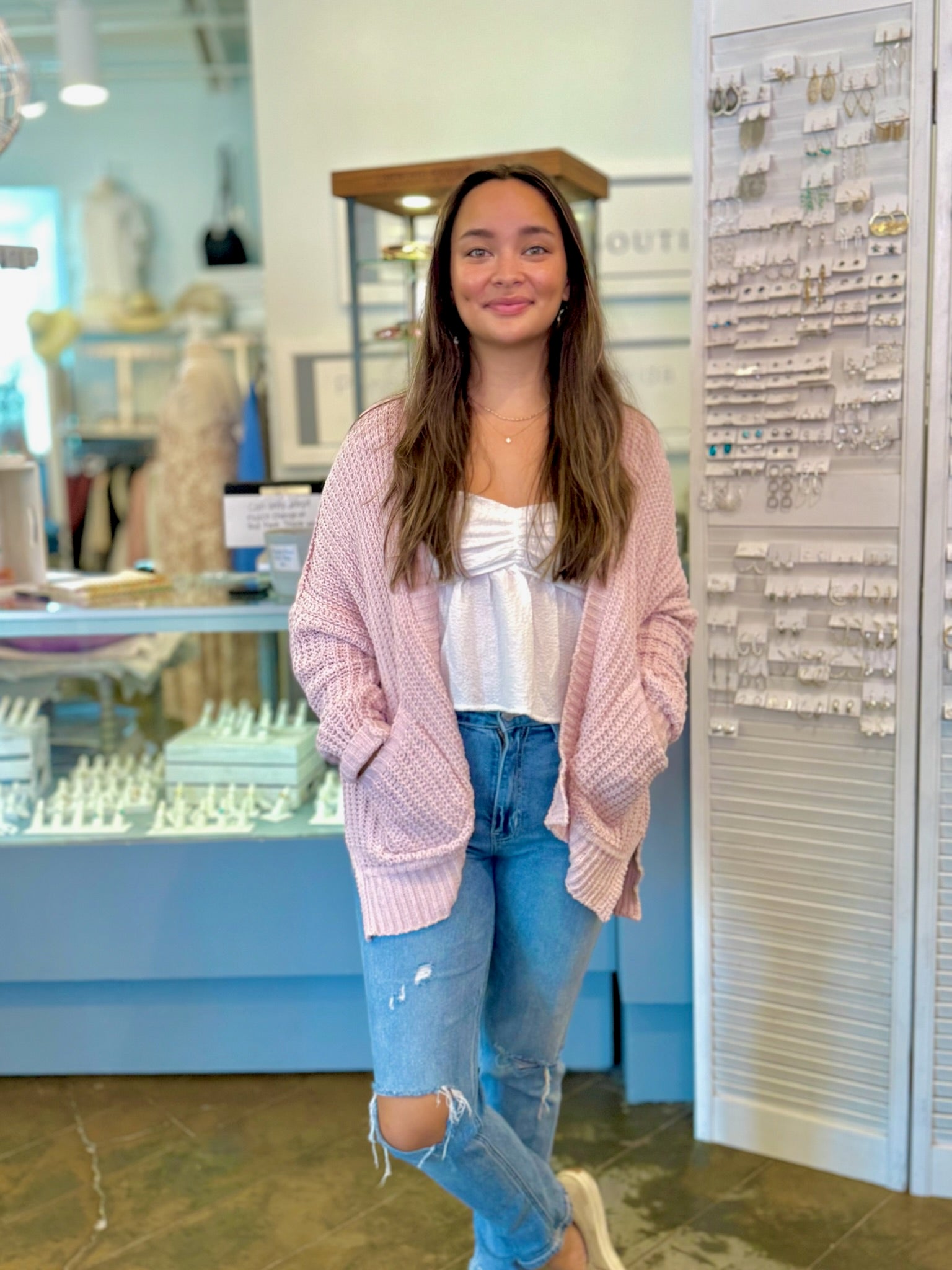 Woman wearing a pink cardigan and blue jeans standing in a store.