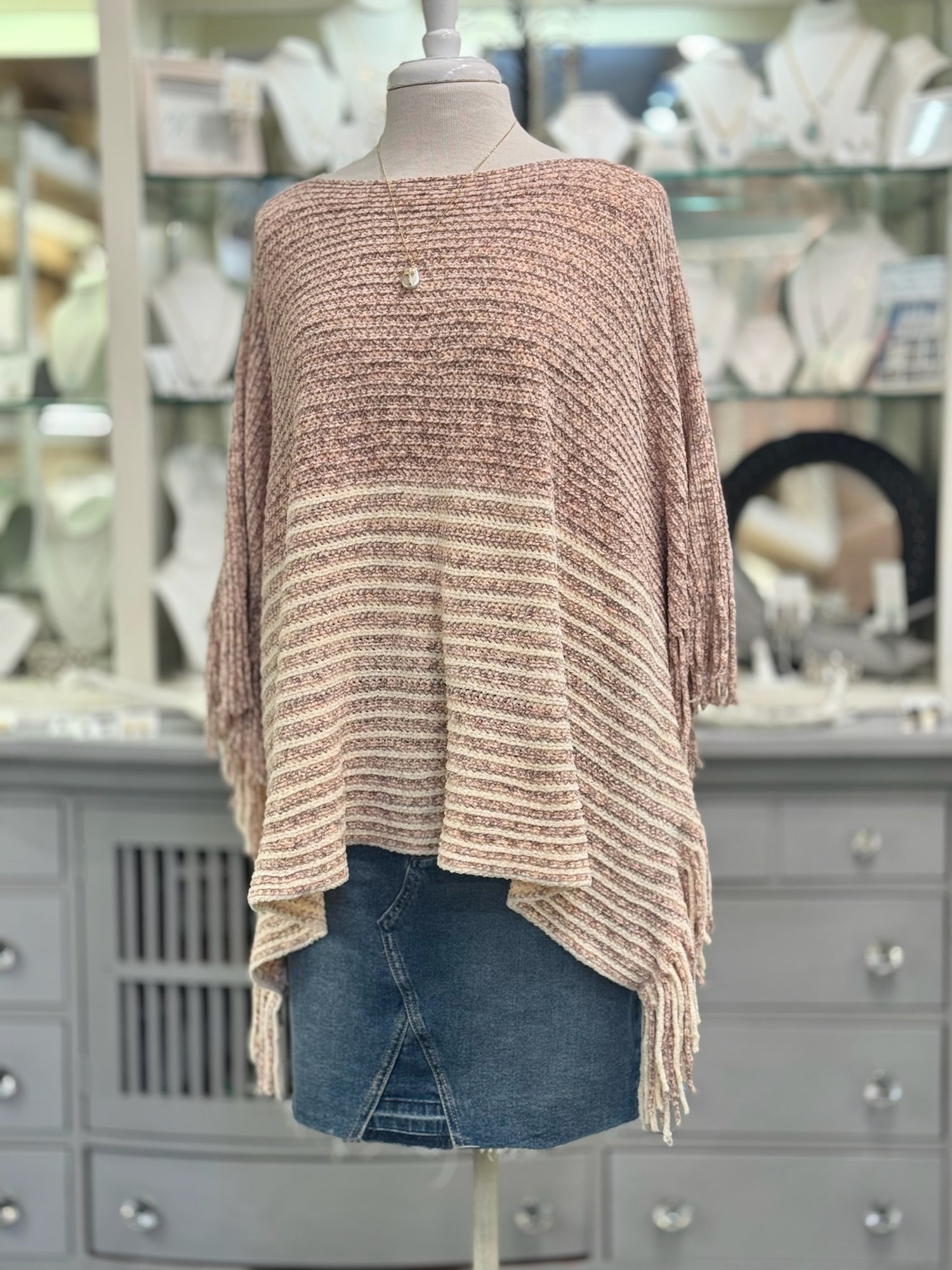 Knitted poncho on a mannequin in front of a store display.