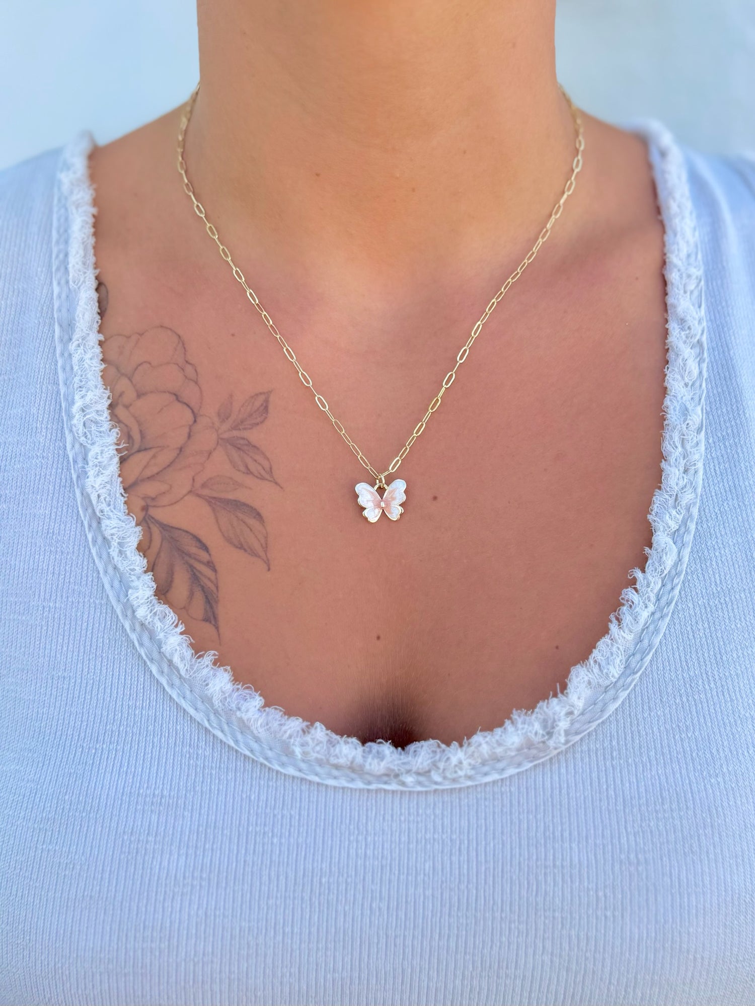 Gold necklace with a butterfly pendant worn by a person against a light blue background