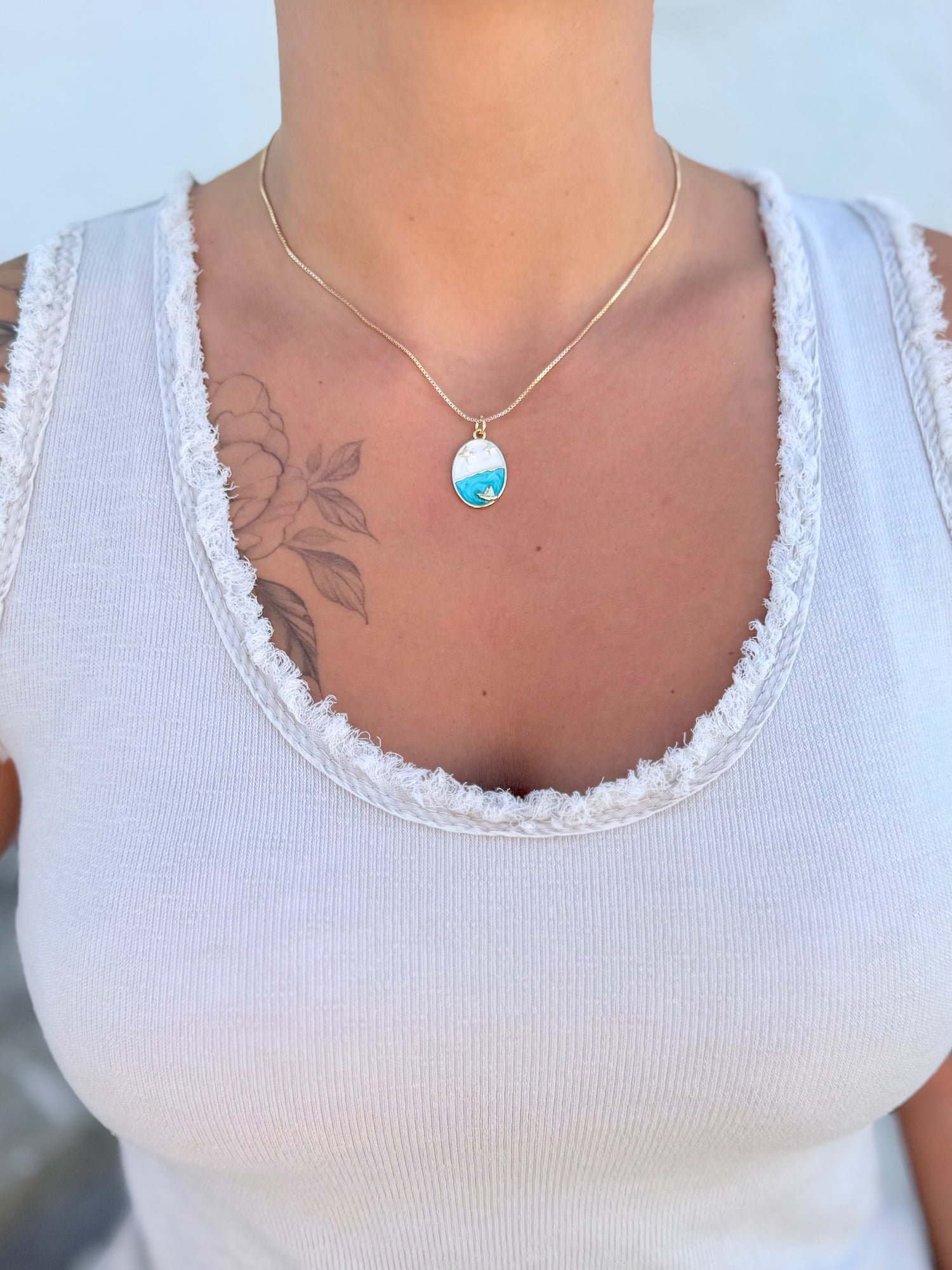 Marina Pendant Necklace with cubic zirconia star accents and golden sailboat on turquoise enamel wave being worn.
