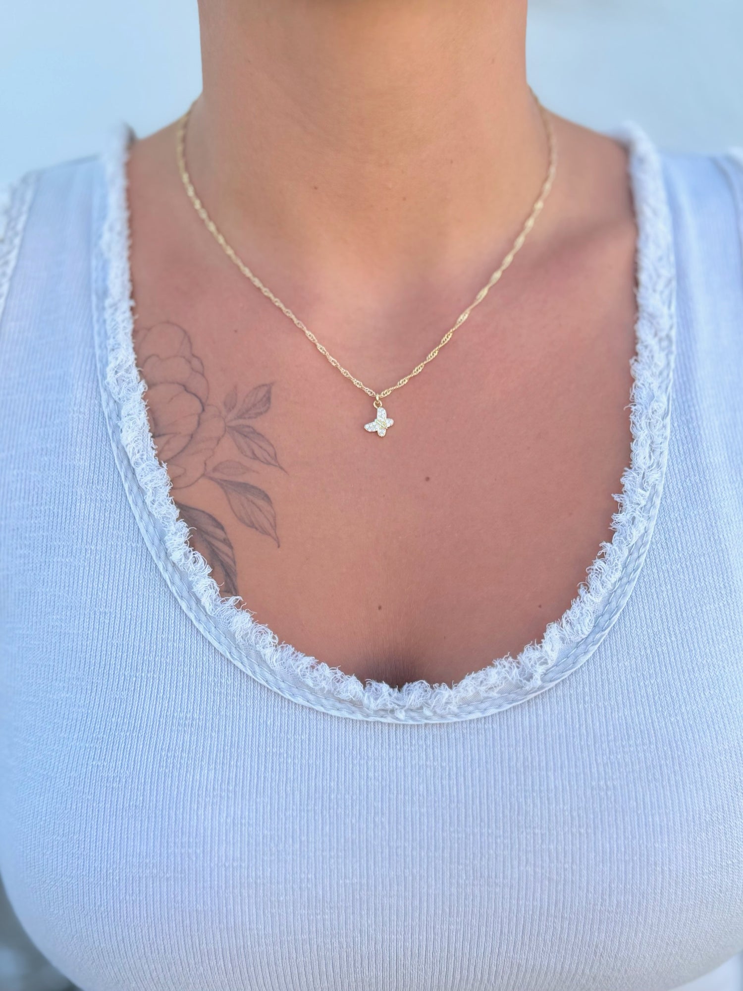 Gold necklace with a butterfly pendant being worn with a light beige shirt