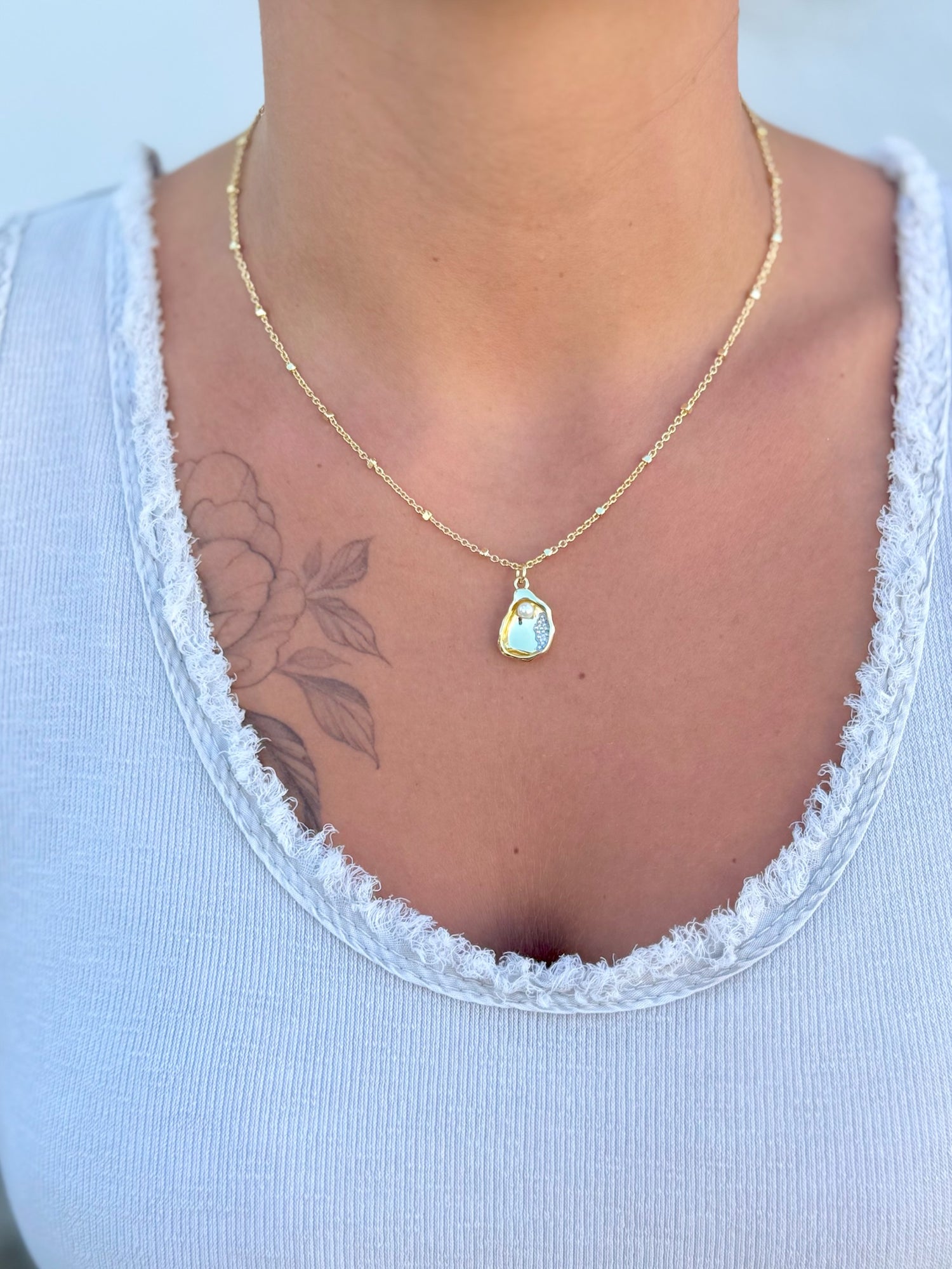 Gold necklace with a pendant featuring a pearl in a golden oyster being worn