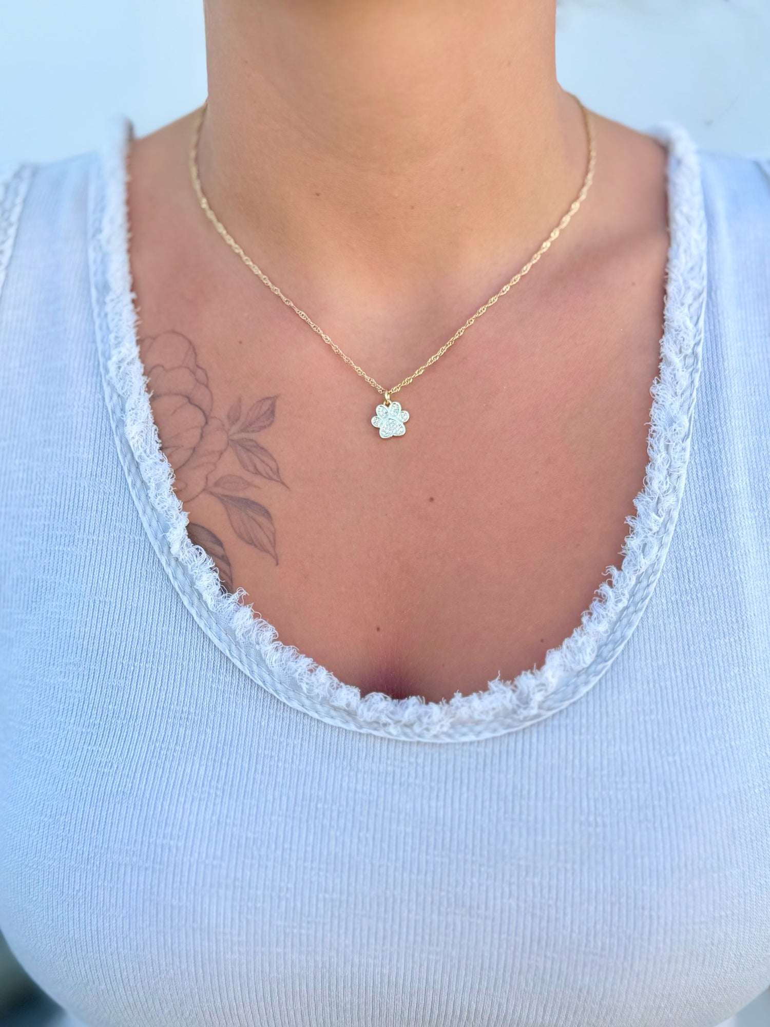 Person wearing a white top with lace trim and a gold necklace with a pendant.