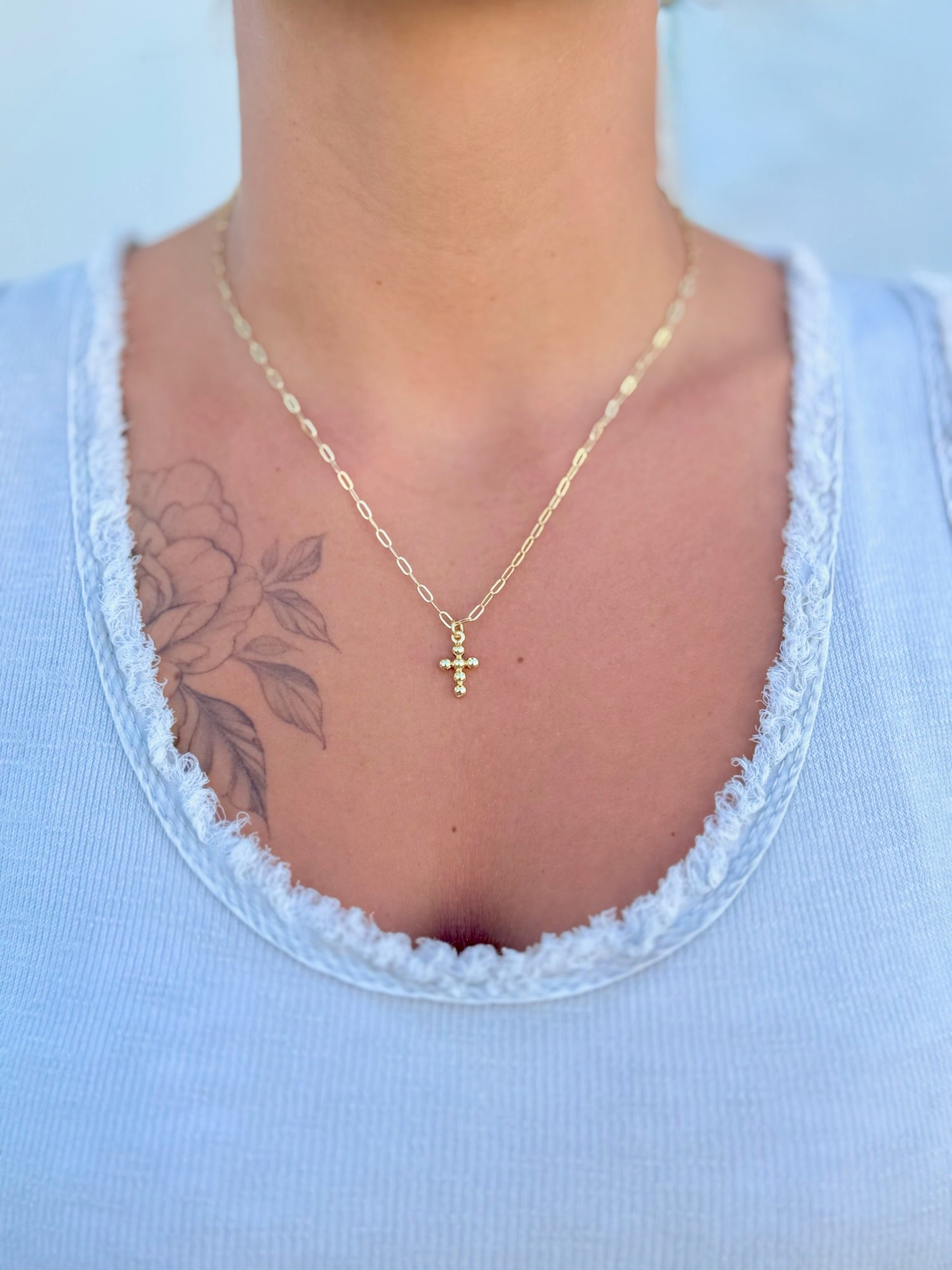 Gold necklace with a cross pendant worn by a person in a light blue top.