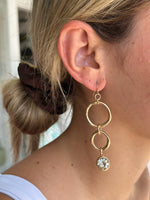 Close-up of a person wearing a gold earring with a clear gemstone.