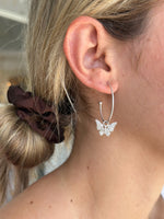 Silver hoop earring with butterfly design worn by a person.