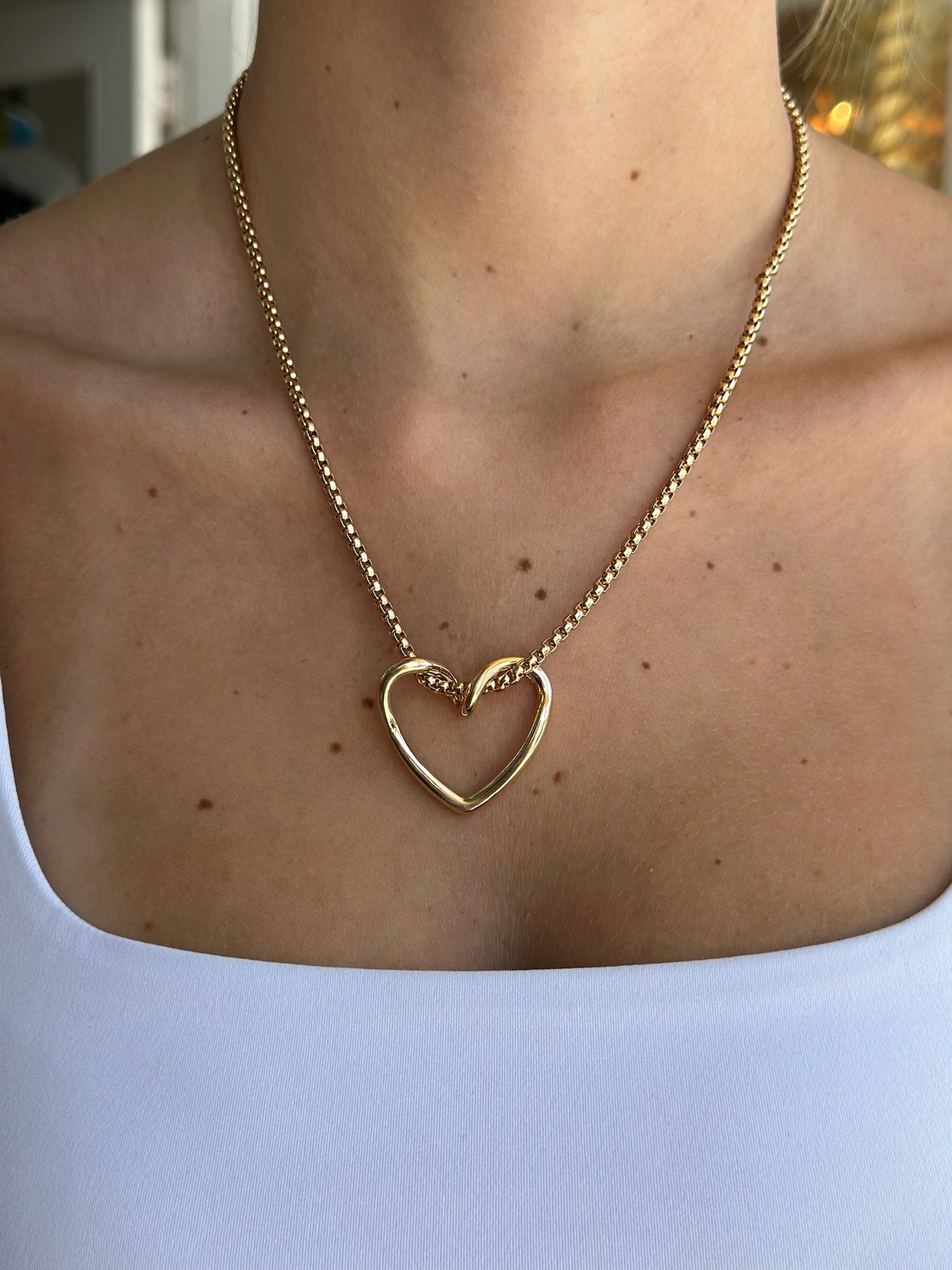 Gold heart-shaped necklace on a person wearing a White  top.
