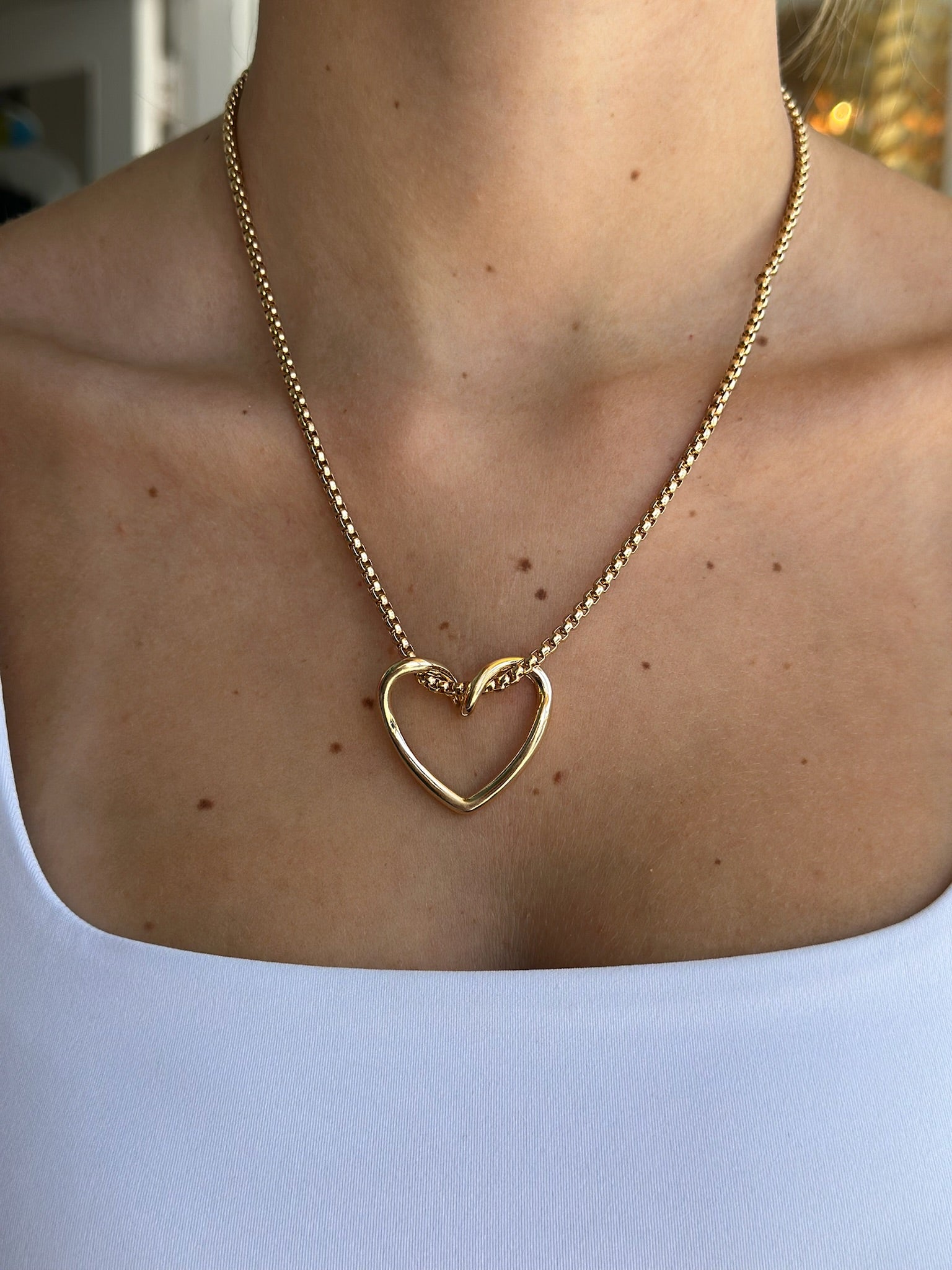 Gold heart-shaped necklace on a person wearing a White top.