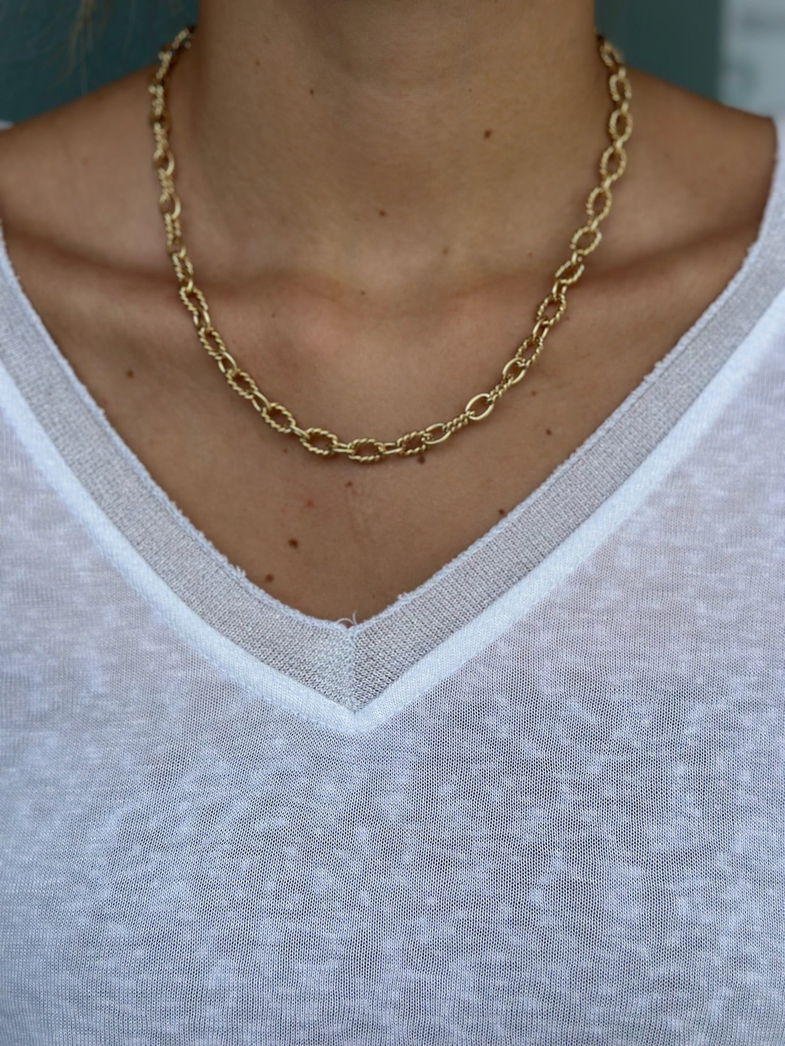 Gold chain necklace worn by a person with a white shirt