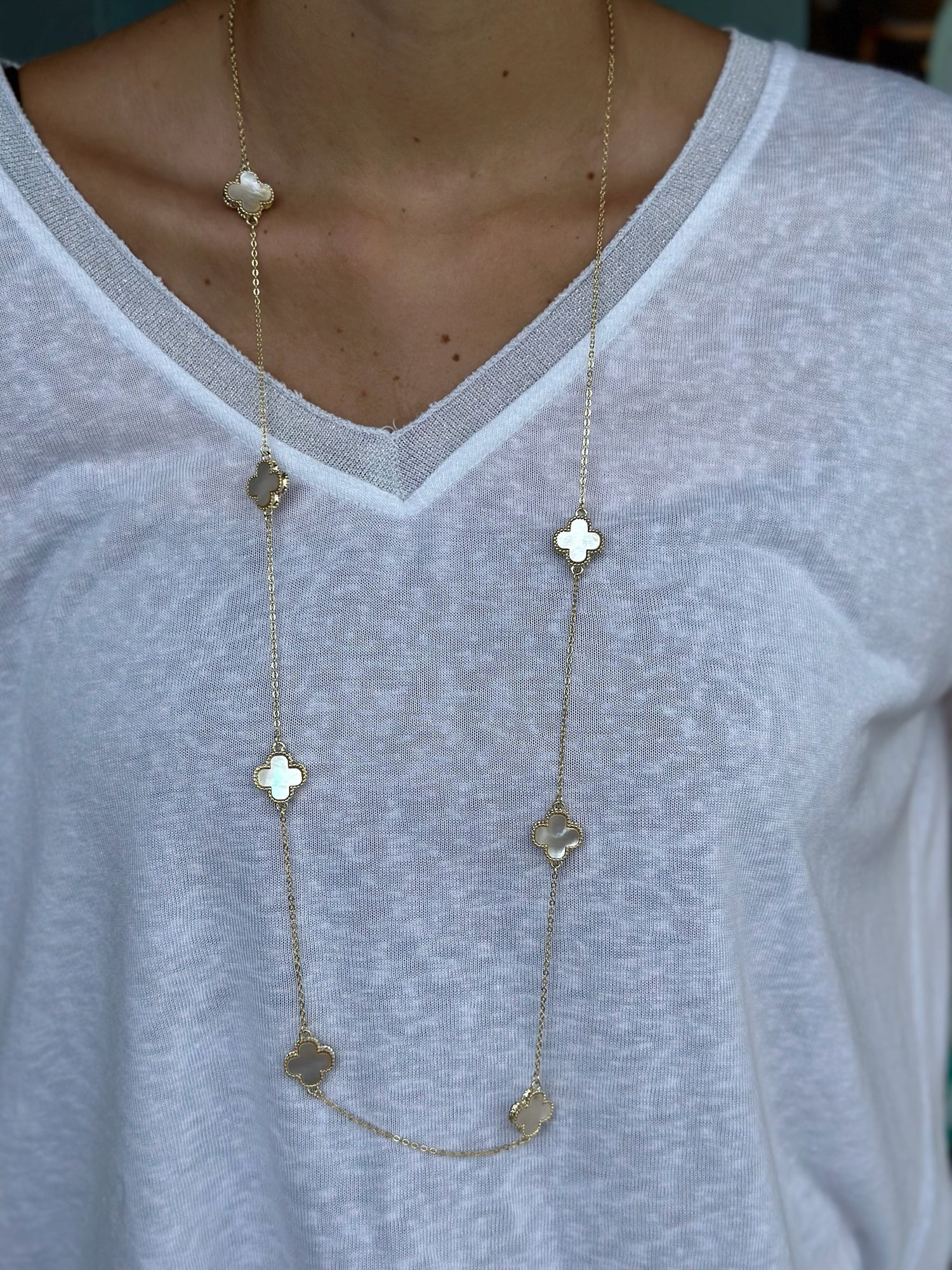 Long gold necklace with clover pendants being worn with a white shirt.