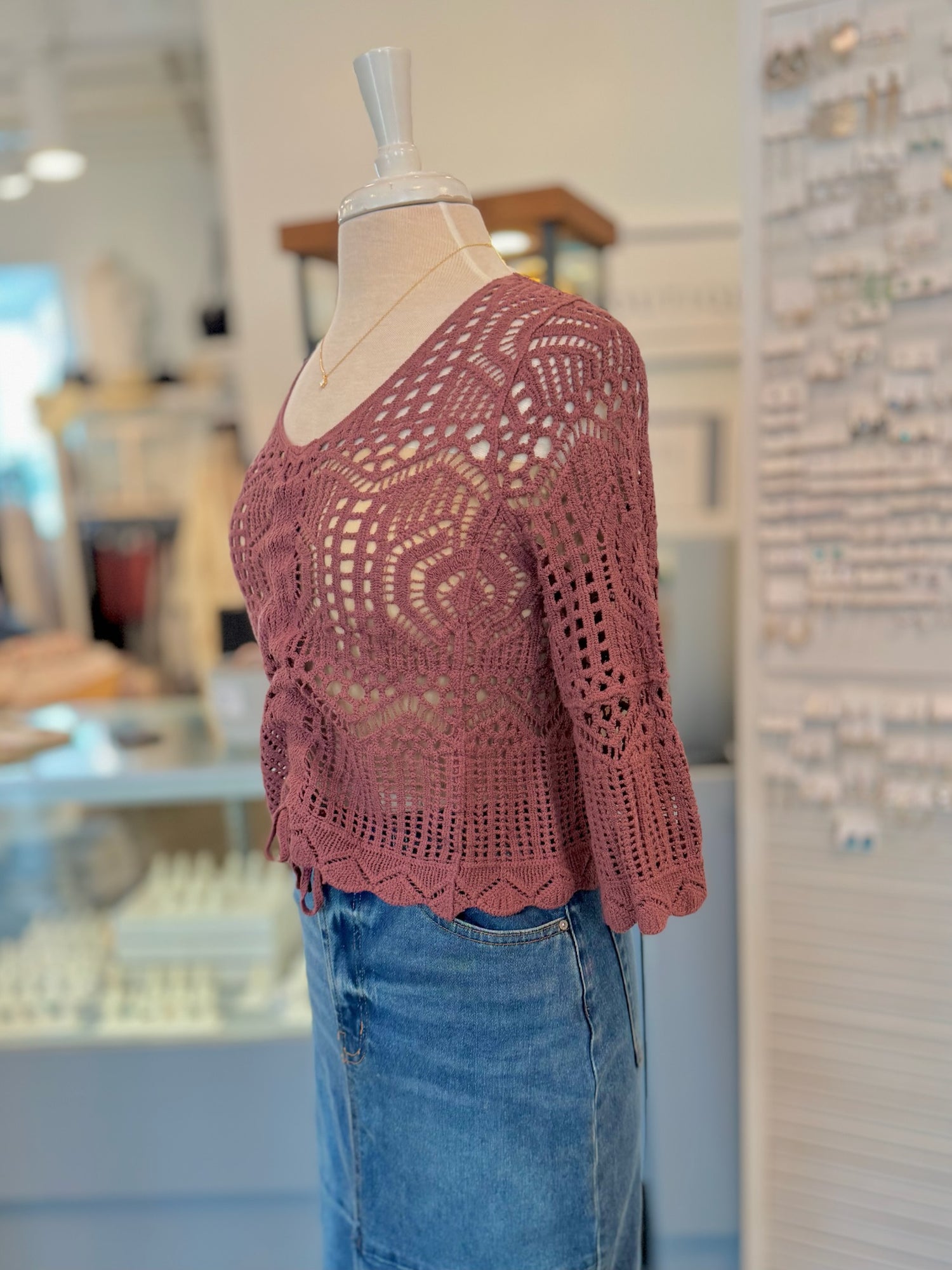 Maroon crochet top on a mannequin with a blurred indoor background