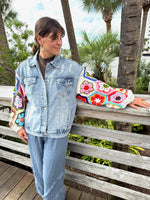Person wearing a denim jacket with colorful arm sleeve, standing outdoors with palm trees in the background.