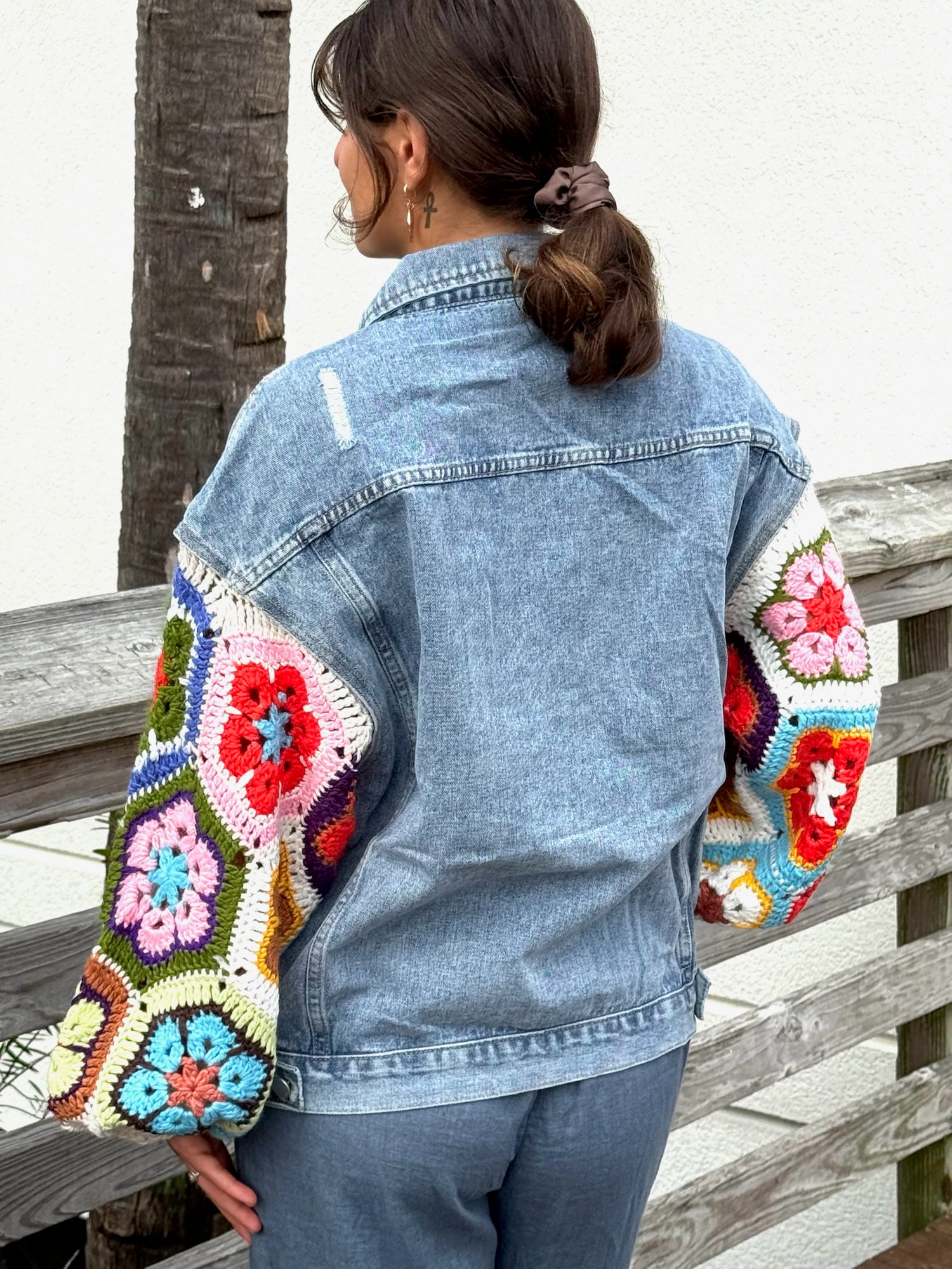 Model wearing a light denim jacket with bright multicolor crochet sleeves