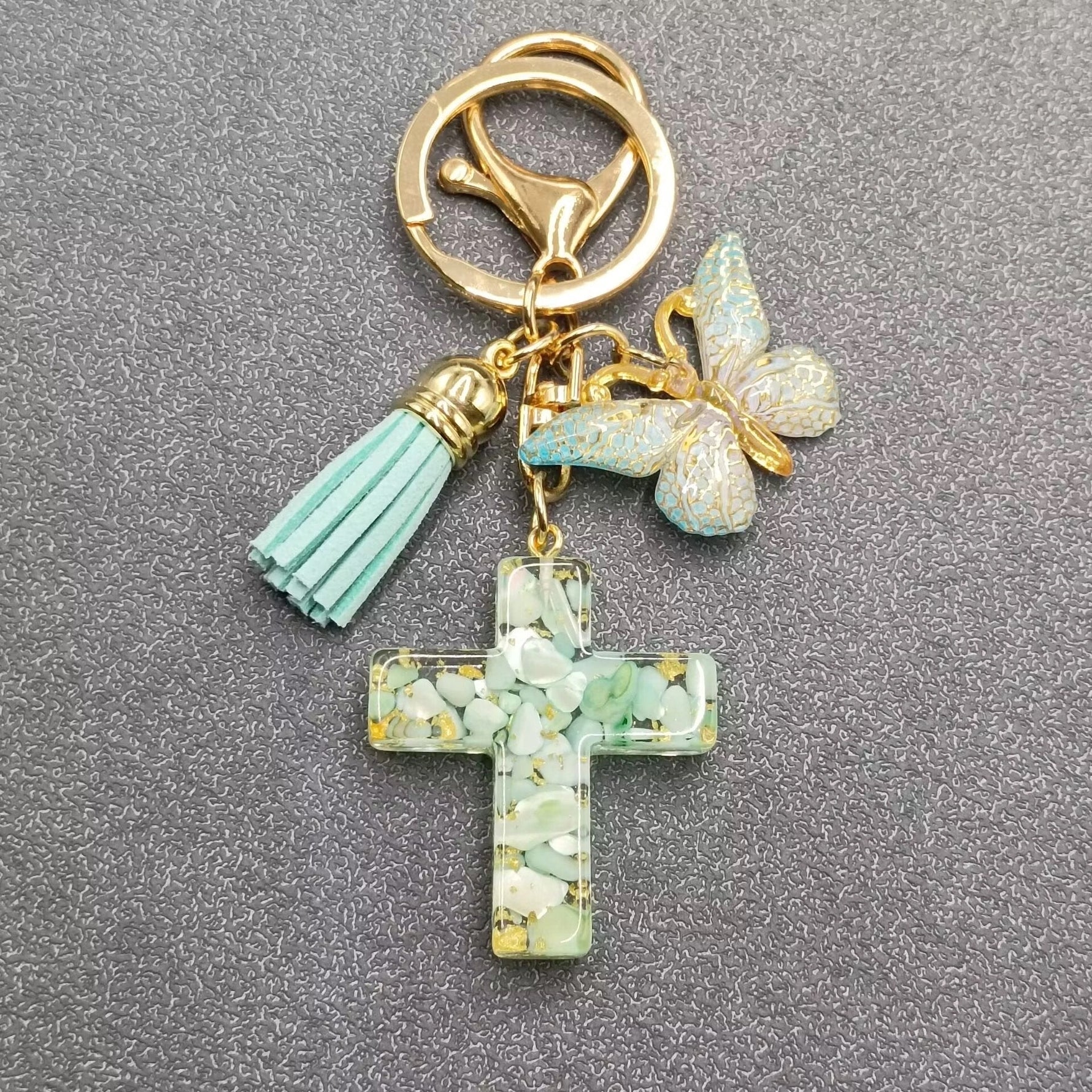 Keychain with cross charm, tassel, and butterfly on a gray background
