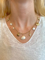 Gold necklace with shell charms worn by a person on a white background