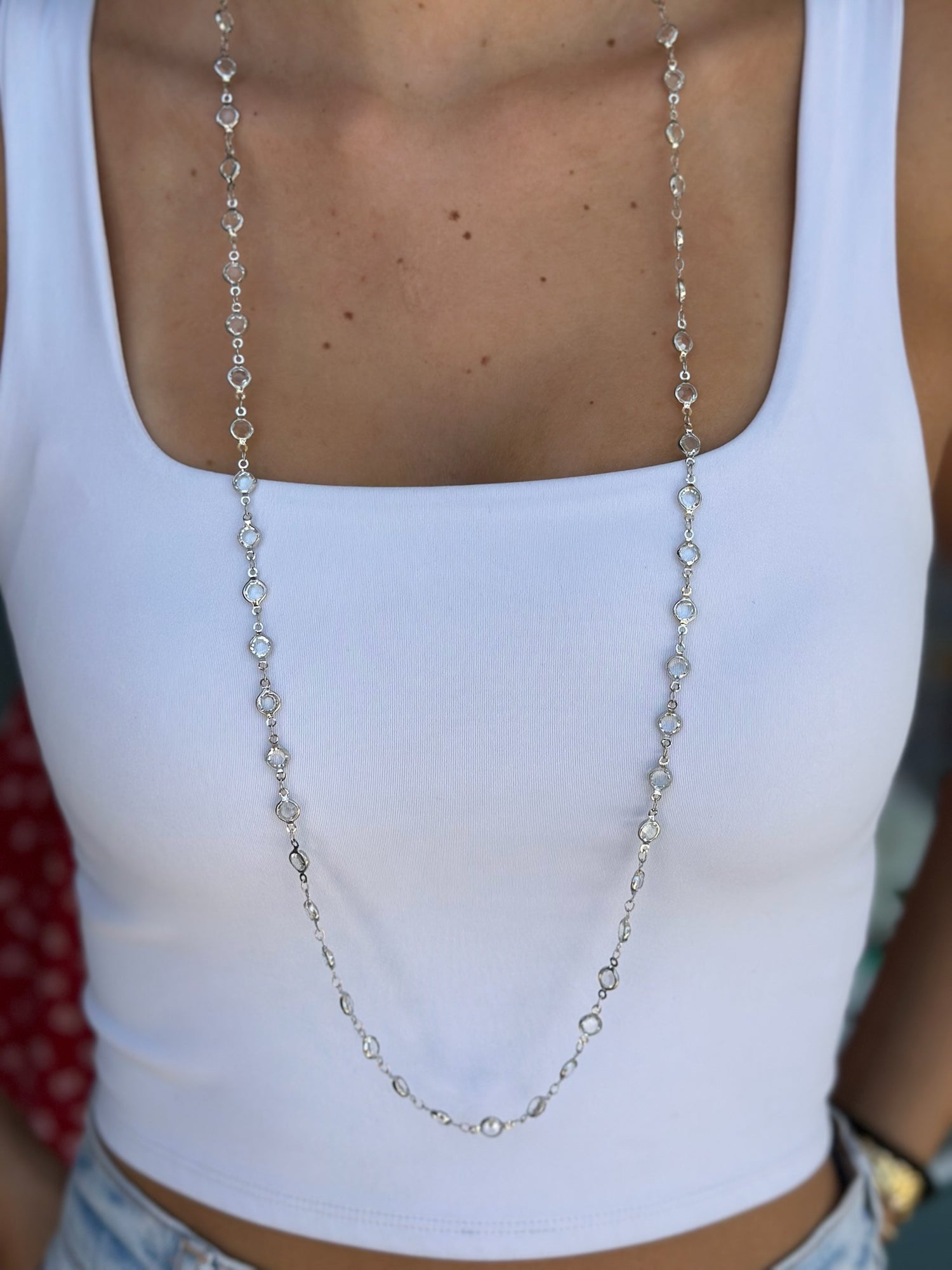 Long silver necklace worn by a person in a white top.