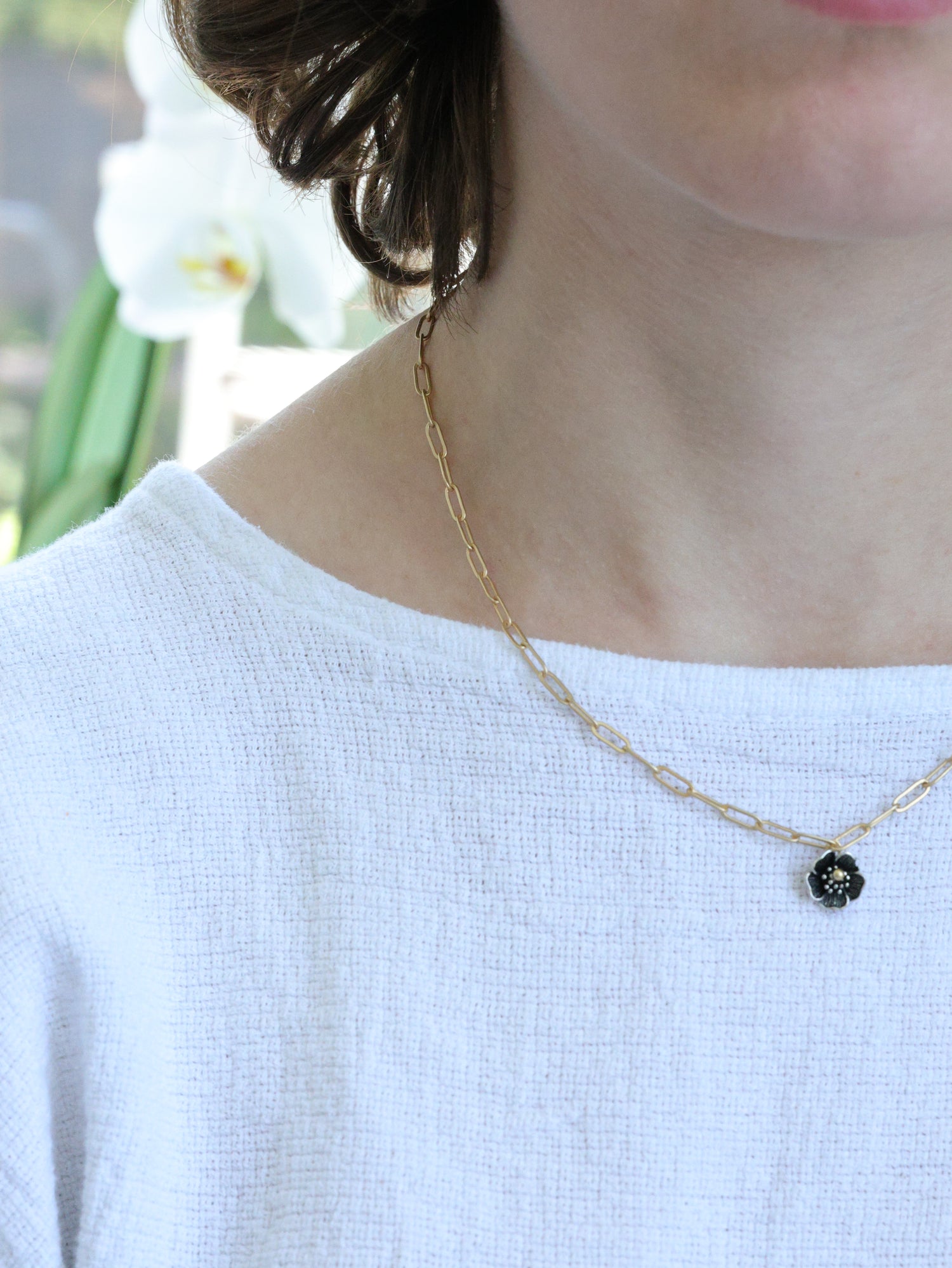 Close-up of a woman wearing a matte gold necklace with a small five-petal flower pendant – minimalist floral jewelry by Ardor Boutique