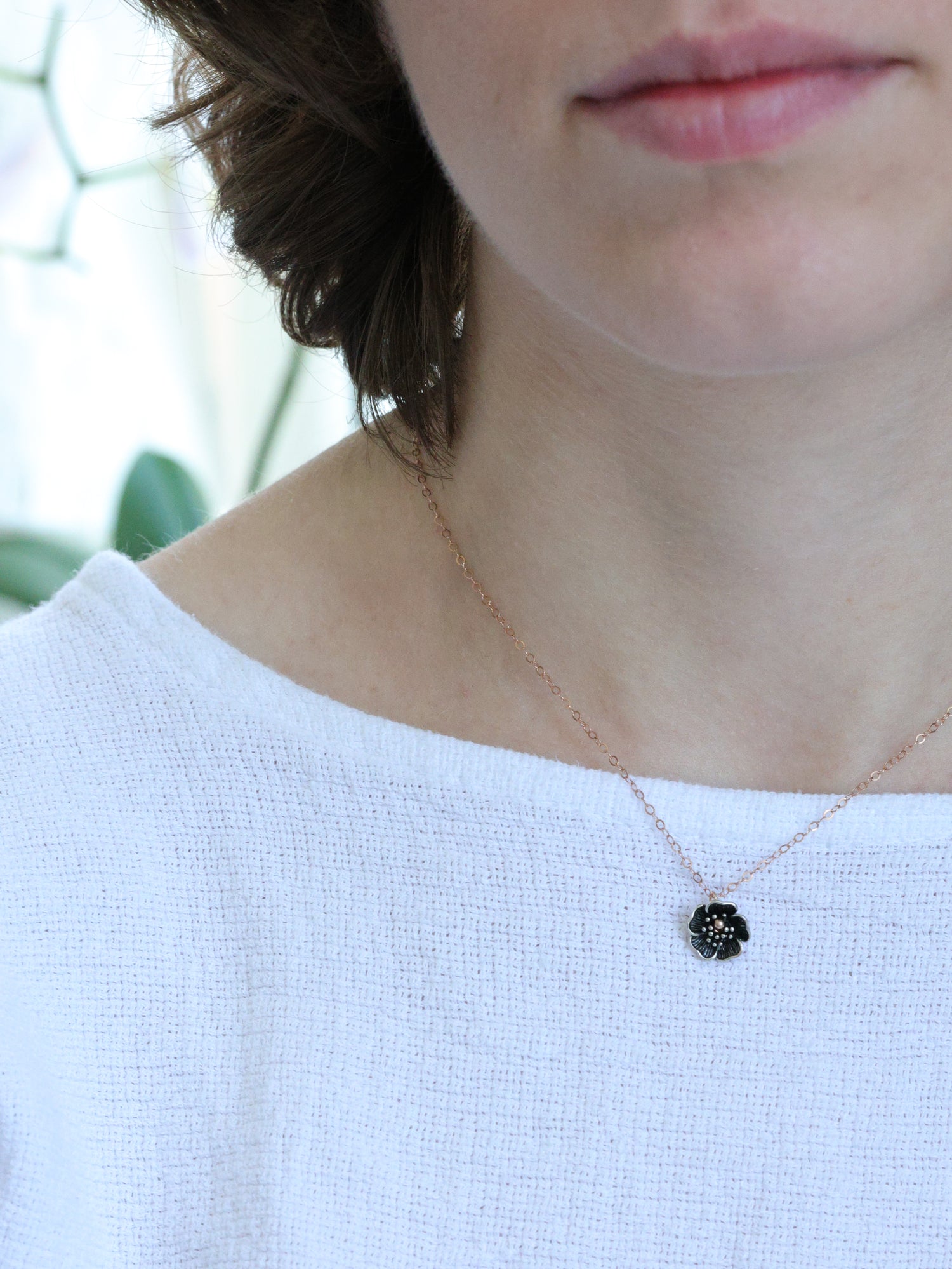 Close-up of a woman wearing a rose gold necklace with a small five-petal flower pendant – minimalist floral jewelry by Ardor Boutique