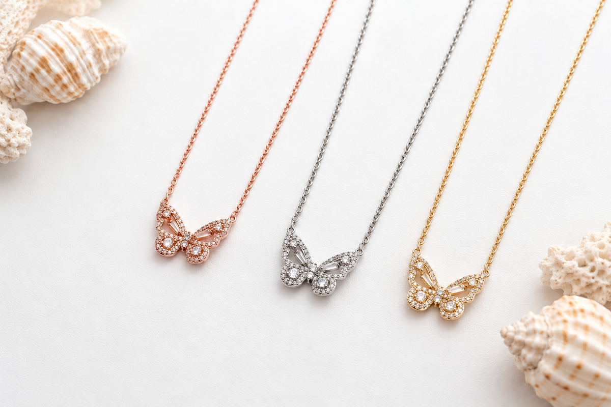Three sparkling butterfly necklaces in rose gold, silver, and gold displayed on a white background with seashell accents at Ardor Boutique.