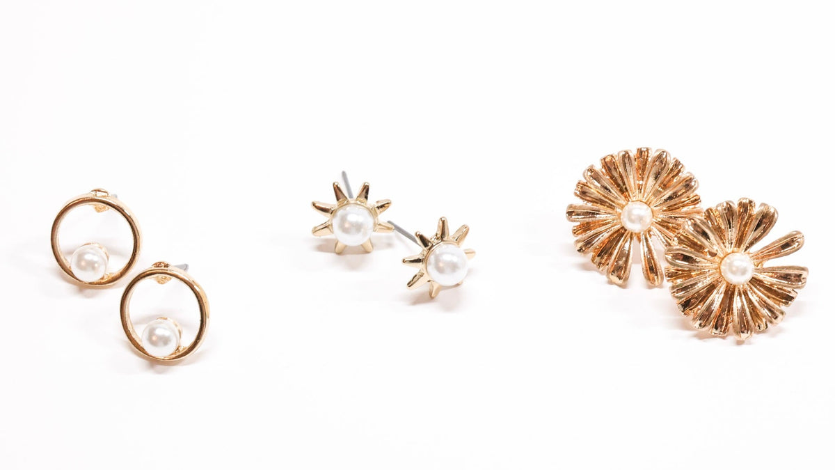 Three pairs of gold-tone stud earrings featuring pearl accents, sunburst designs, and textured floral shapes, displayed on a white background for the Stud Earrings collection at Ardor Boutique.