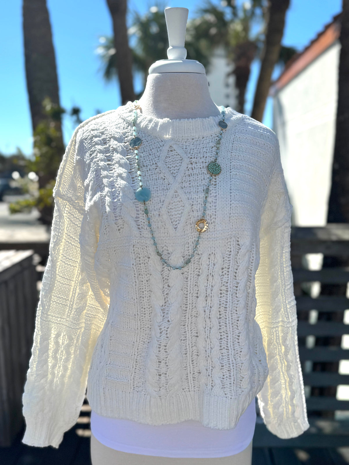 Ivory cable knit sweater with a crew neckline, long sleeves, textured knit patterns, and ribbed trim, styled with a turquoise beaded necklace at Ardor Boutique.