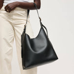 Black leather handbag held by a person wearing beige pants on a light background
