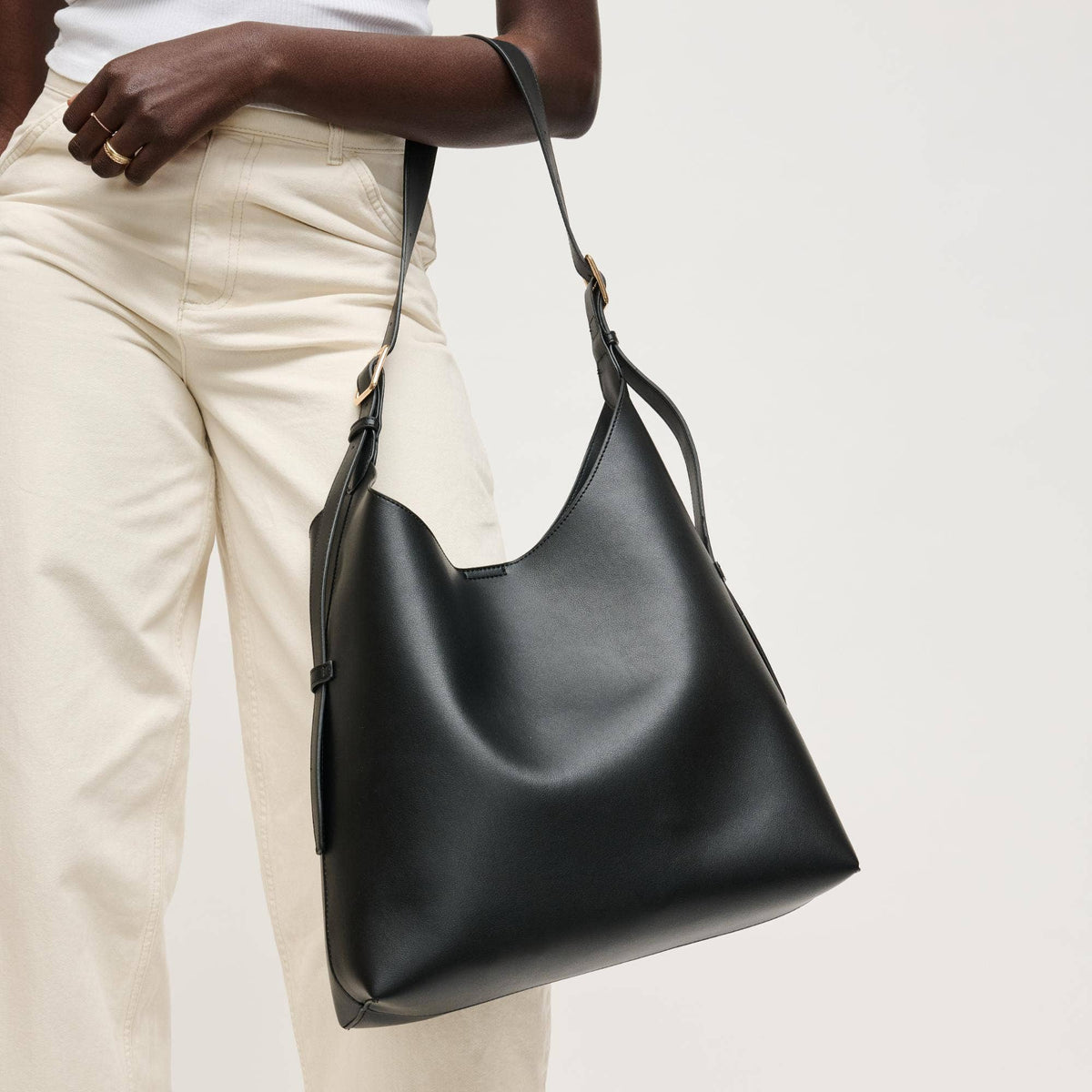Black leather handbag held by a person wearing beige pants on a light background
