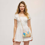 A woman modeling a white short-sleeve smocked dress with a colorful embroidered crossbody bag featuring a bird pattern, set against a plain light gray studio background.