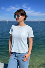 Person wearing sunglasses and a light blue shirt by a body of water