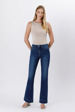 Model wearing high-rise bootcut jeans with a tailored hem and sleeveless beige top.