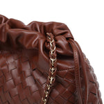 Close-up of a brown woven handbag with a drawstring and gold chain detail.