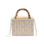Wicker handbag with bamboo handle and pearl embellishments on a white background