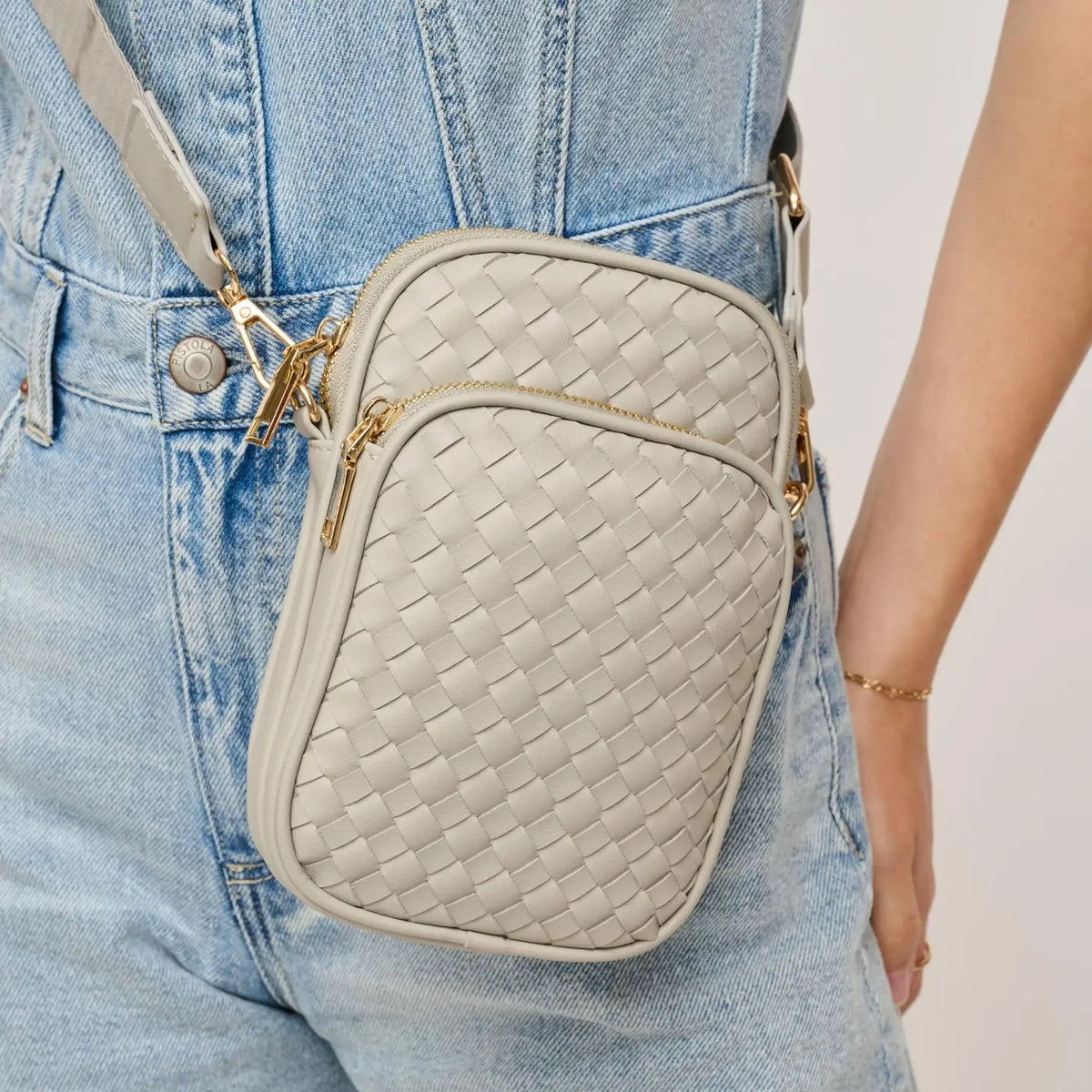 A light Grey crossbody bag with gold-tone hardware, worn crossbody over light-wash denim overalls.