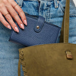Blue leather wallet held by a hand against a denim background