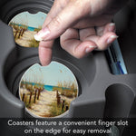 Coaster with a scenic design being removed from a holder with text 'Coasters feature a convenient finger slot on the edge for easy removal'.